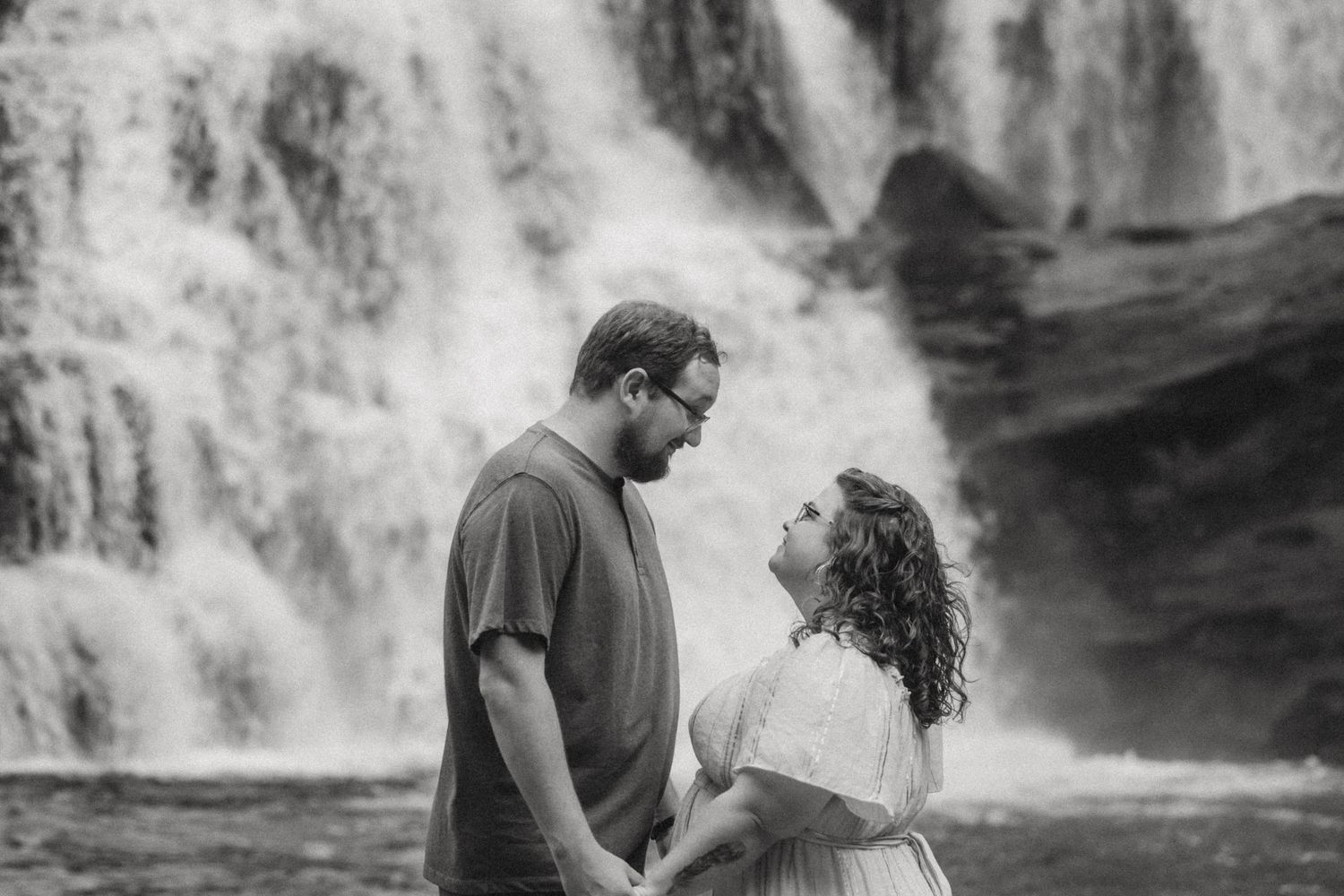 A romantic couple embraces near a cascading waterfall during an outdoor photo shoot.