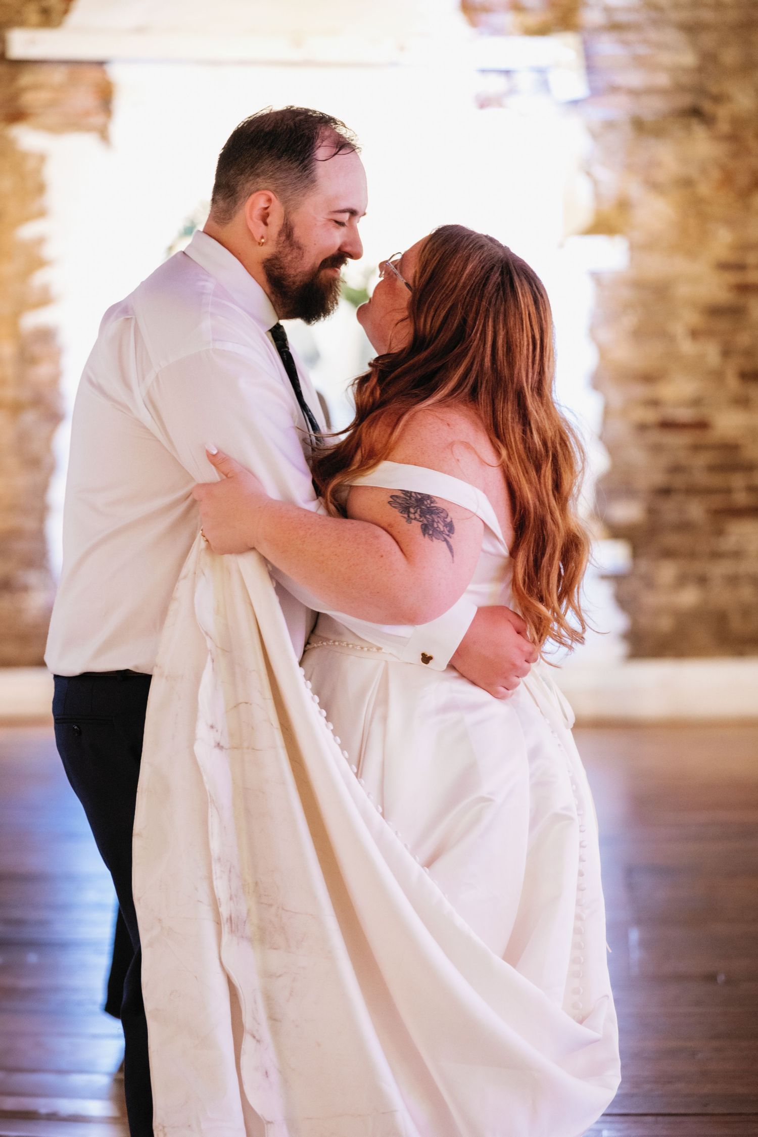 A couple shares their first dance together in a rustic brick-walled venue with soft lighting.
