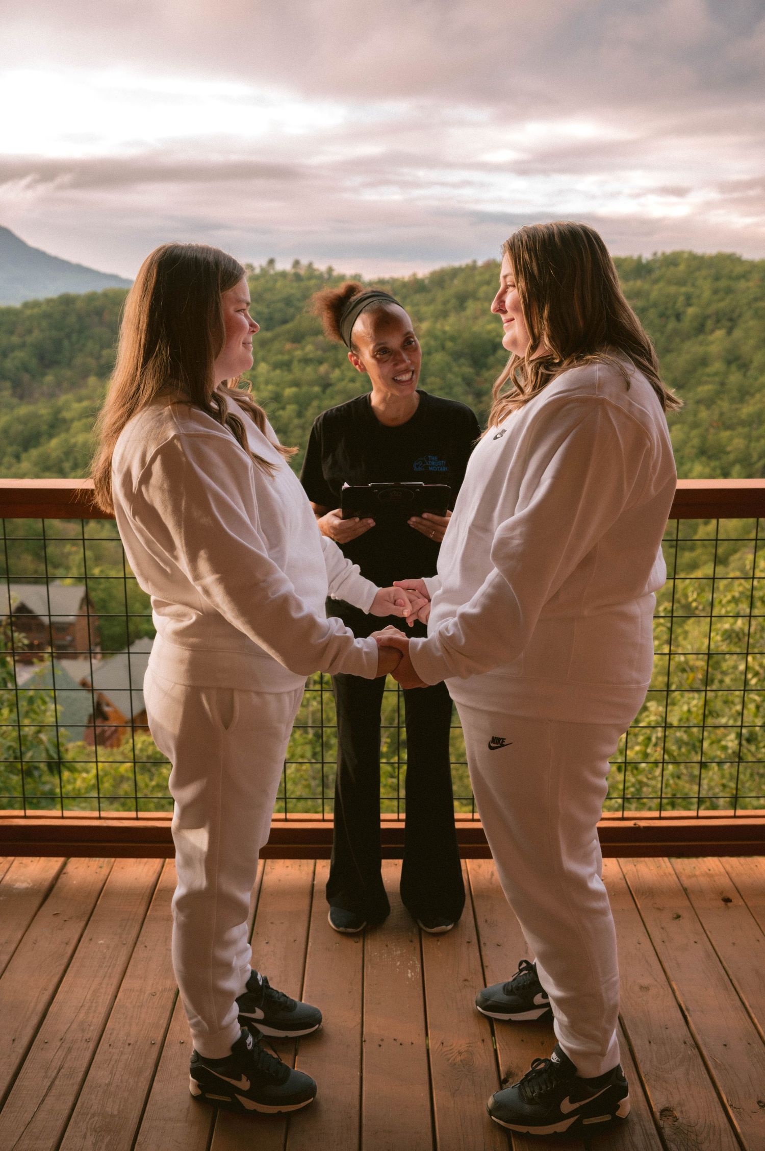 Children in white outfits play together on a wooden deck overlooking scenic mountain views at sunset.
