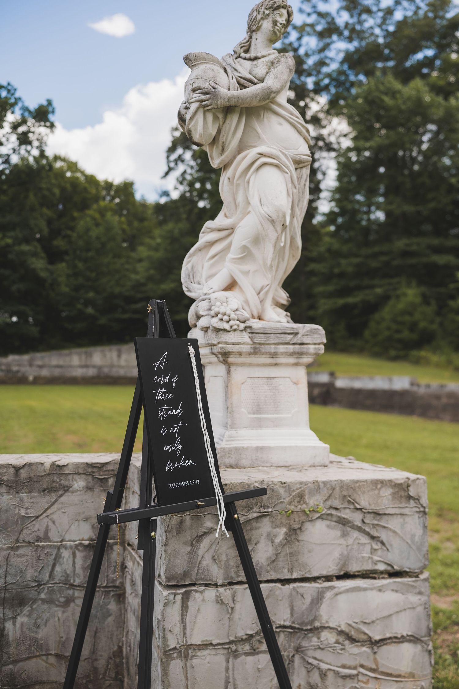 Decorative white stone statue stands atop marble wall with black chalkboard signs for a wedding.