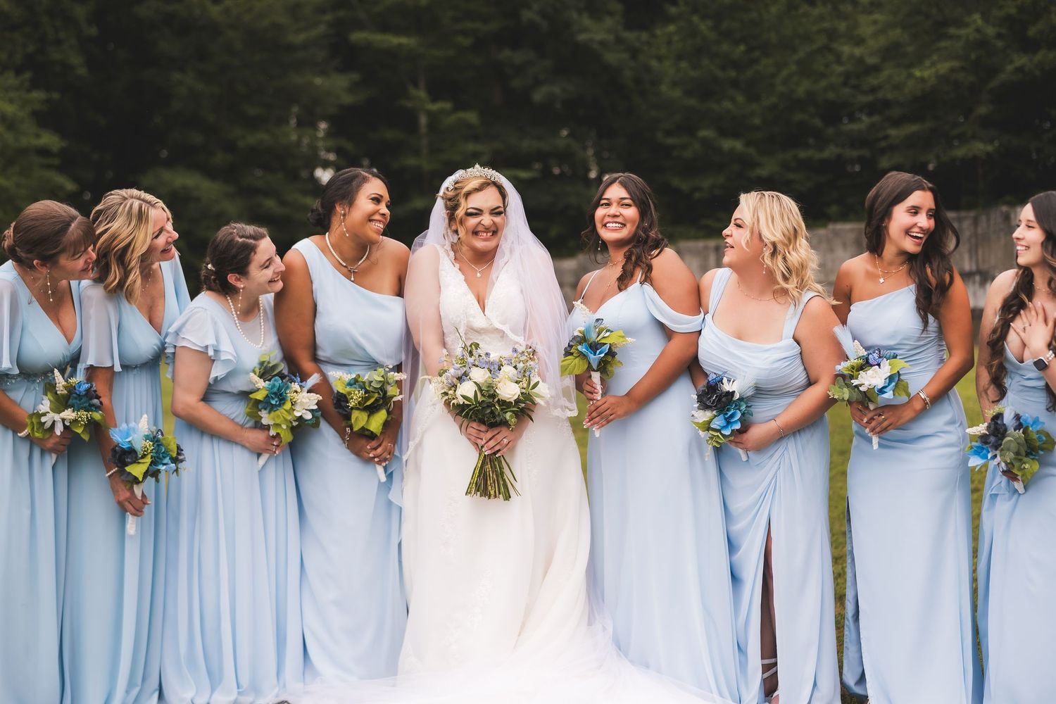 A wedding party lineup with bridesmaids in light blue dresses holding colorful bouquets.
