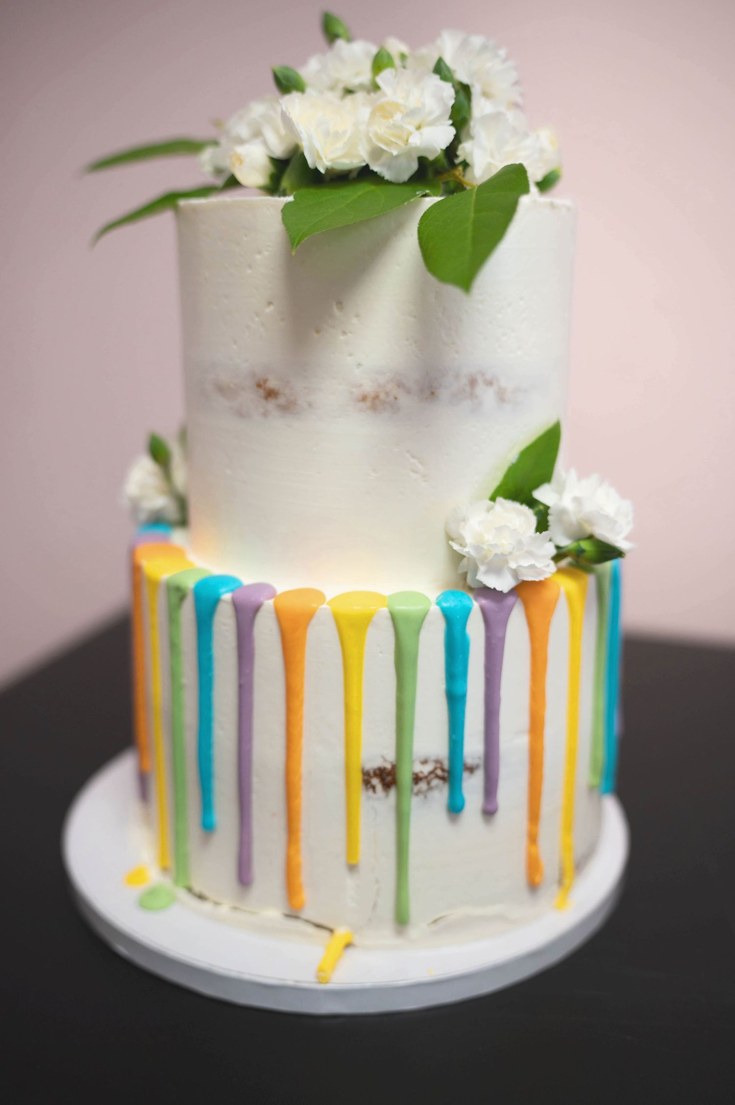 Two-tier white wedding cake decorated with colorful drips and fresh white flowers on top.