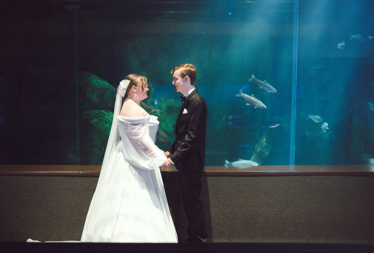 A couple shares their first dance in front of a large aquarium tank with blue lighting.