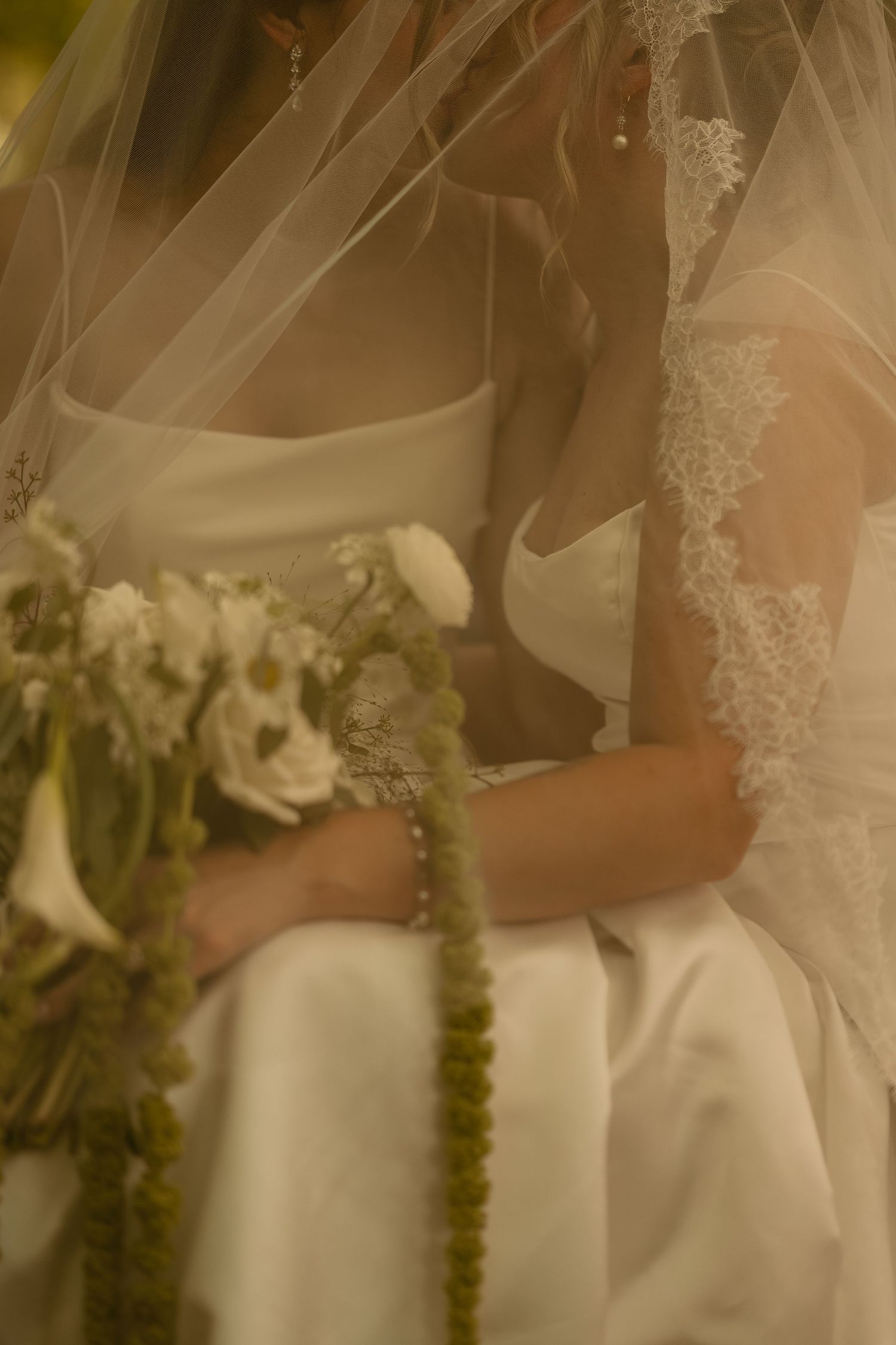 Close-up detail of delicate lace veil and white floral bouquet elements in soft sepia tones.