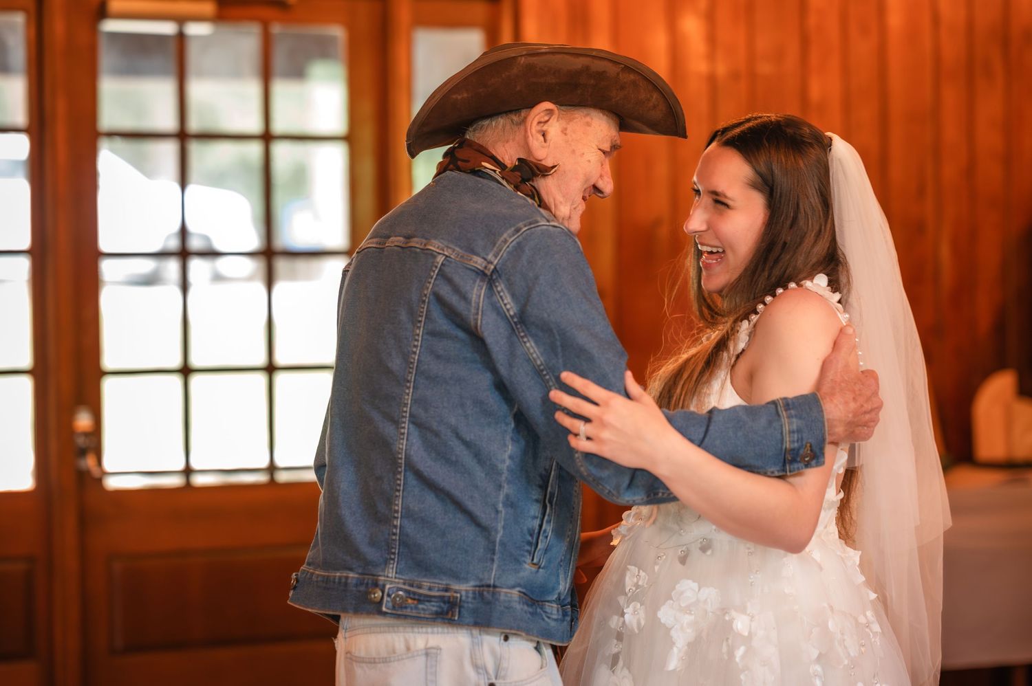 A couple shares an intimate moment during their rustic barn wedding ceremony with wooden walls and windows.