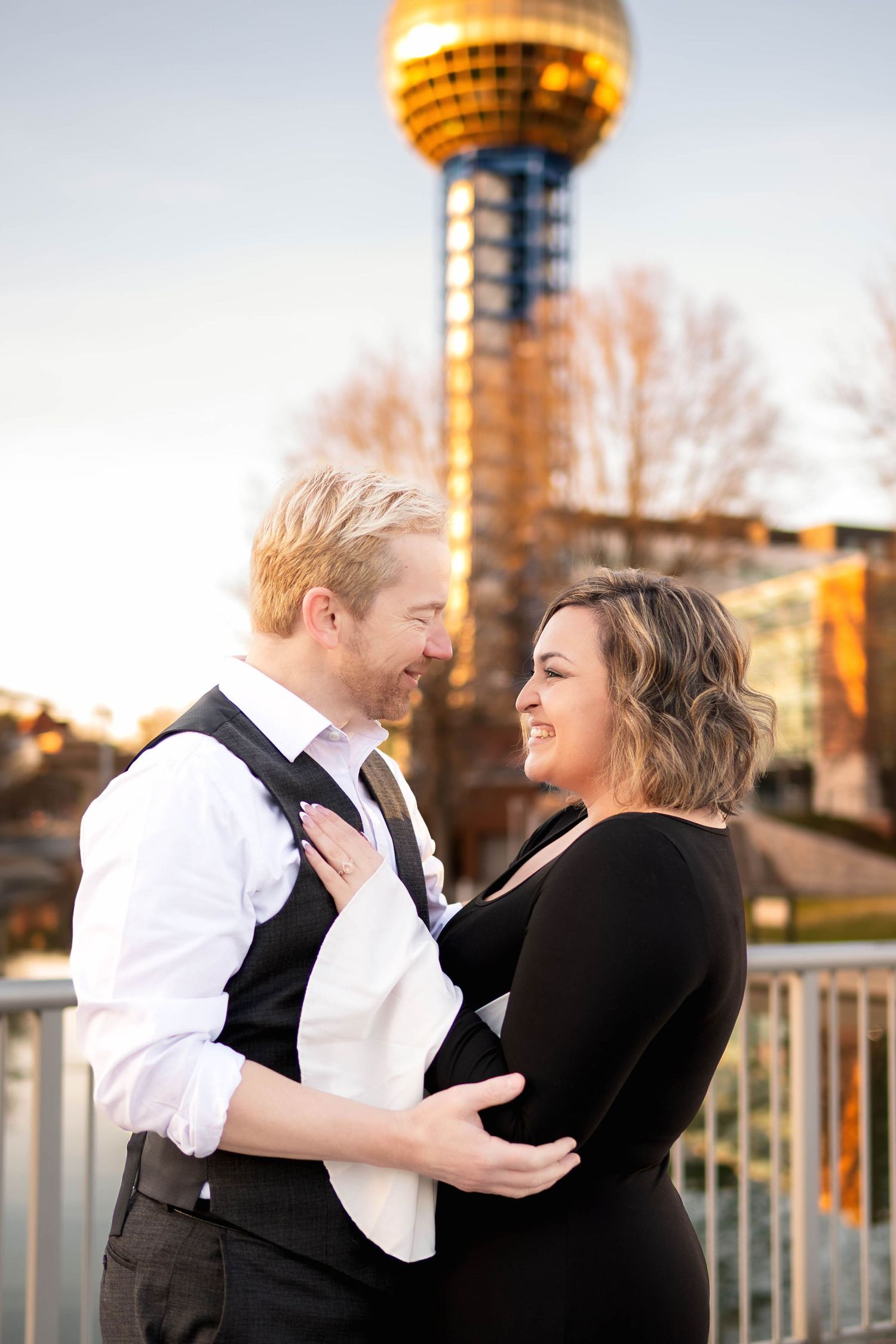 A romantic couple dressed in formal attire dance together at sunset on an urban rooftop with a golden tower in the background.