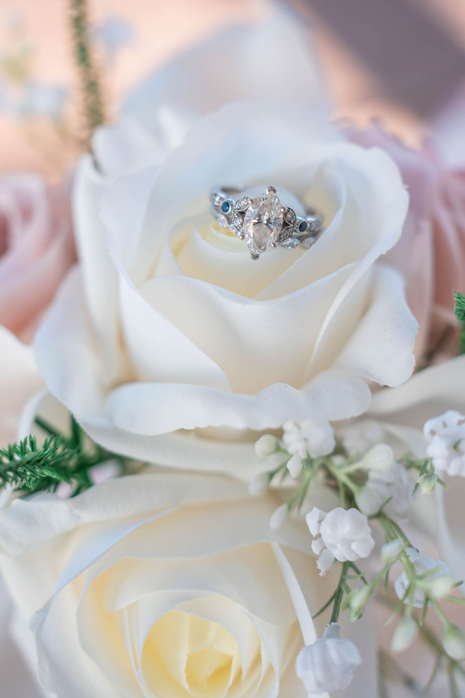 Elegant white roses adorned with delicate baby's breath and sparkling engagement ring in soft natural lighting.