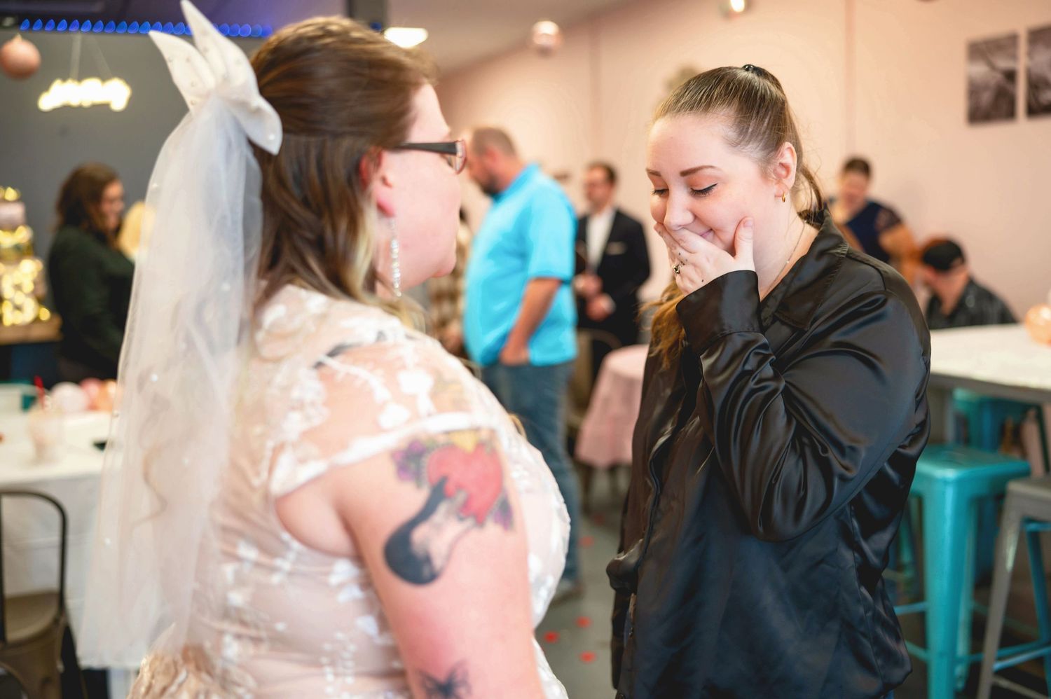 An emotional candid moment between a bride in a lace dress with tattoos and someone in a navy sweater at a reception.
