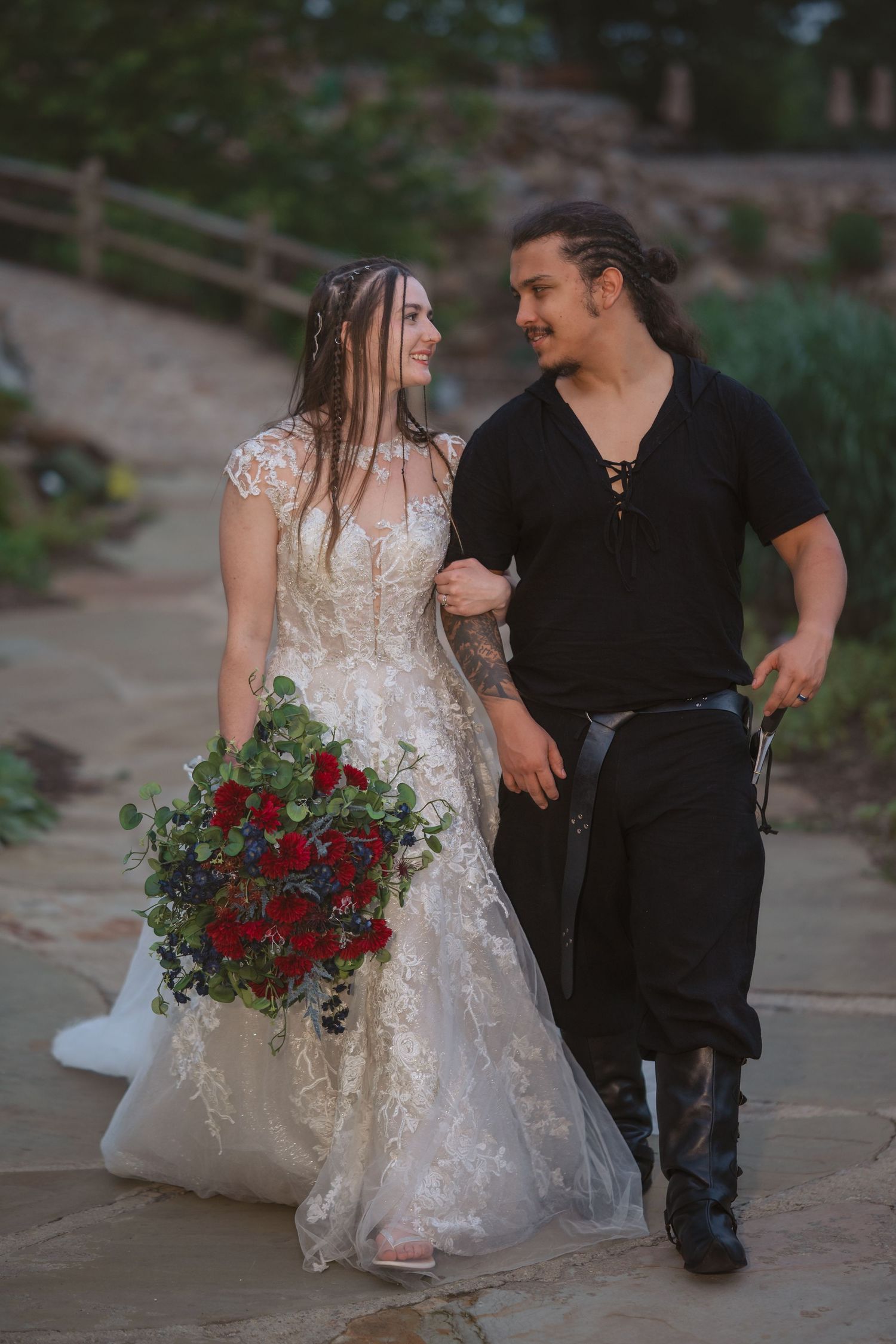 A couple sits together on stone steps with red roses and a white wedding dress creating a romantic scene.