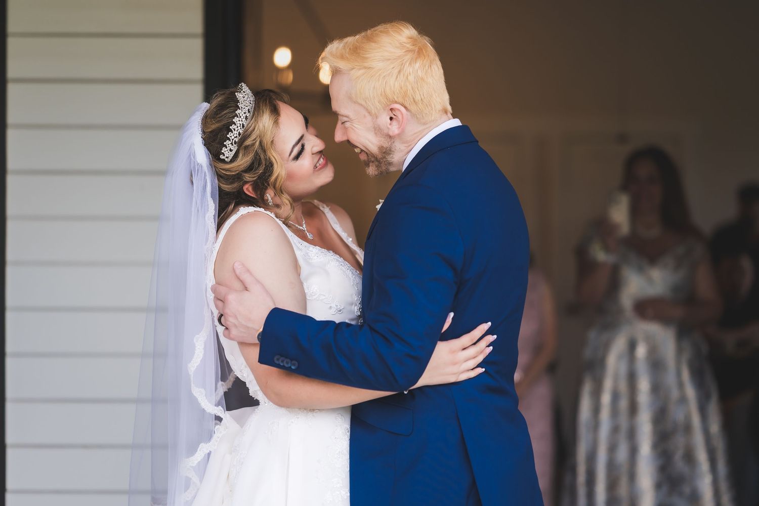 Two people sharing a romantic kiss at an indoor venue with white walls.