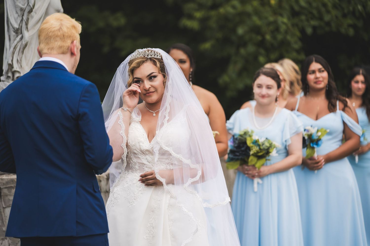 Wedding party in light blue bridesmaid dresses poses with bride in white gown during outdoor celebration.