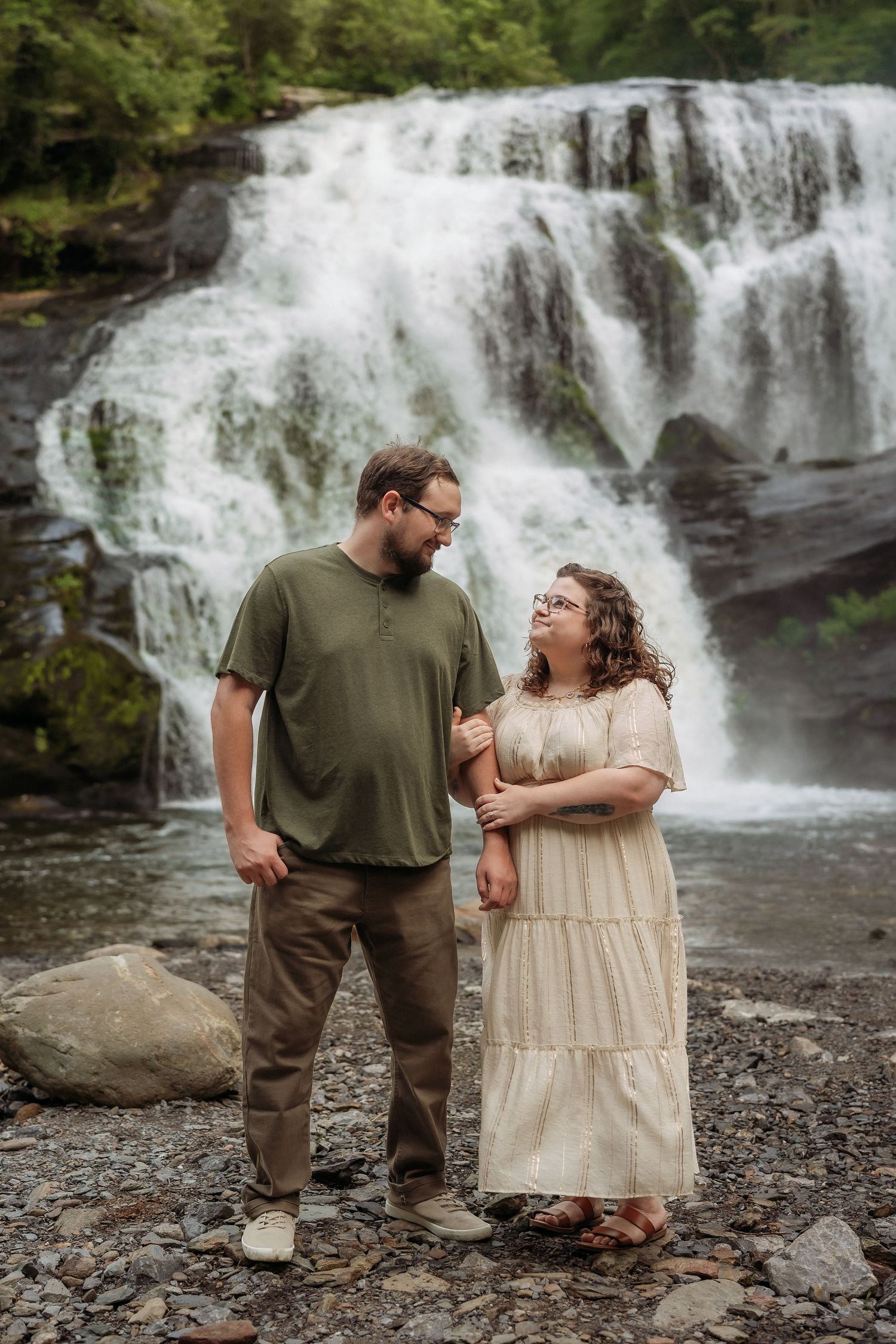 A couple shares an intimate moment by a cascading waterfall in a scenic forest setting.