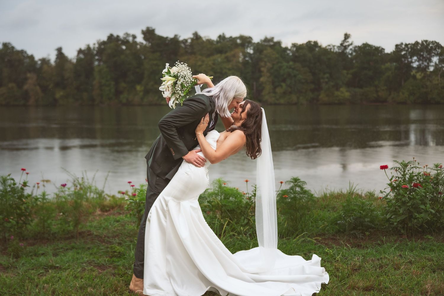 Romantic waterfront wedding ceremony setup with white chairs and floral decorations by a lake.