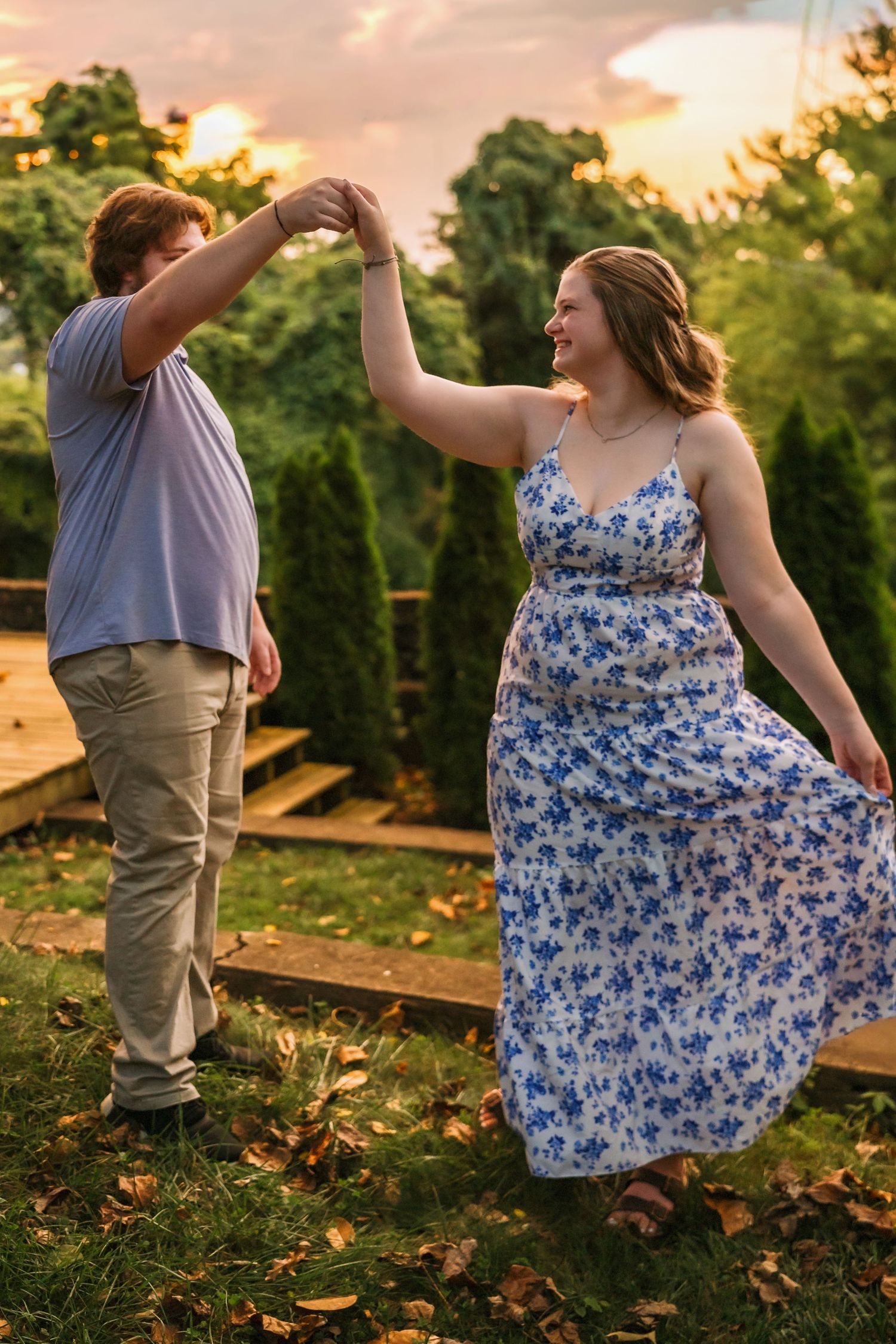 Golden sunset light illuminates couple dancing playfully outdoors among fallen autumn leaves.