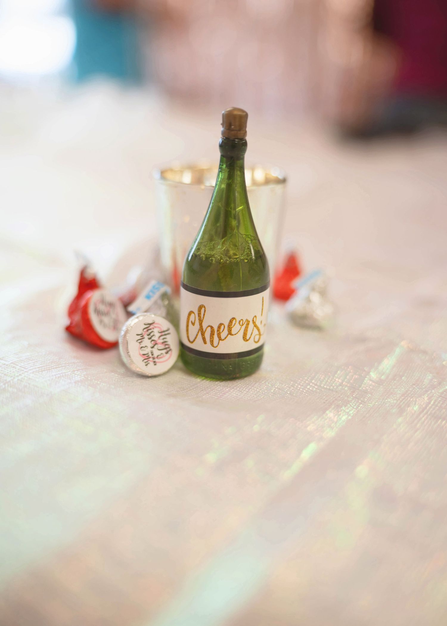 Small decorative bottle with 'Cheers' written on it displayed with party favors on a wooden surface.