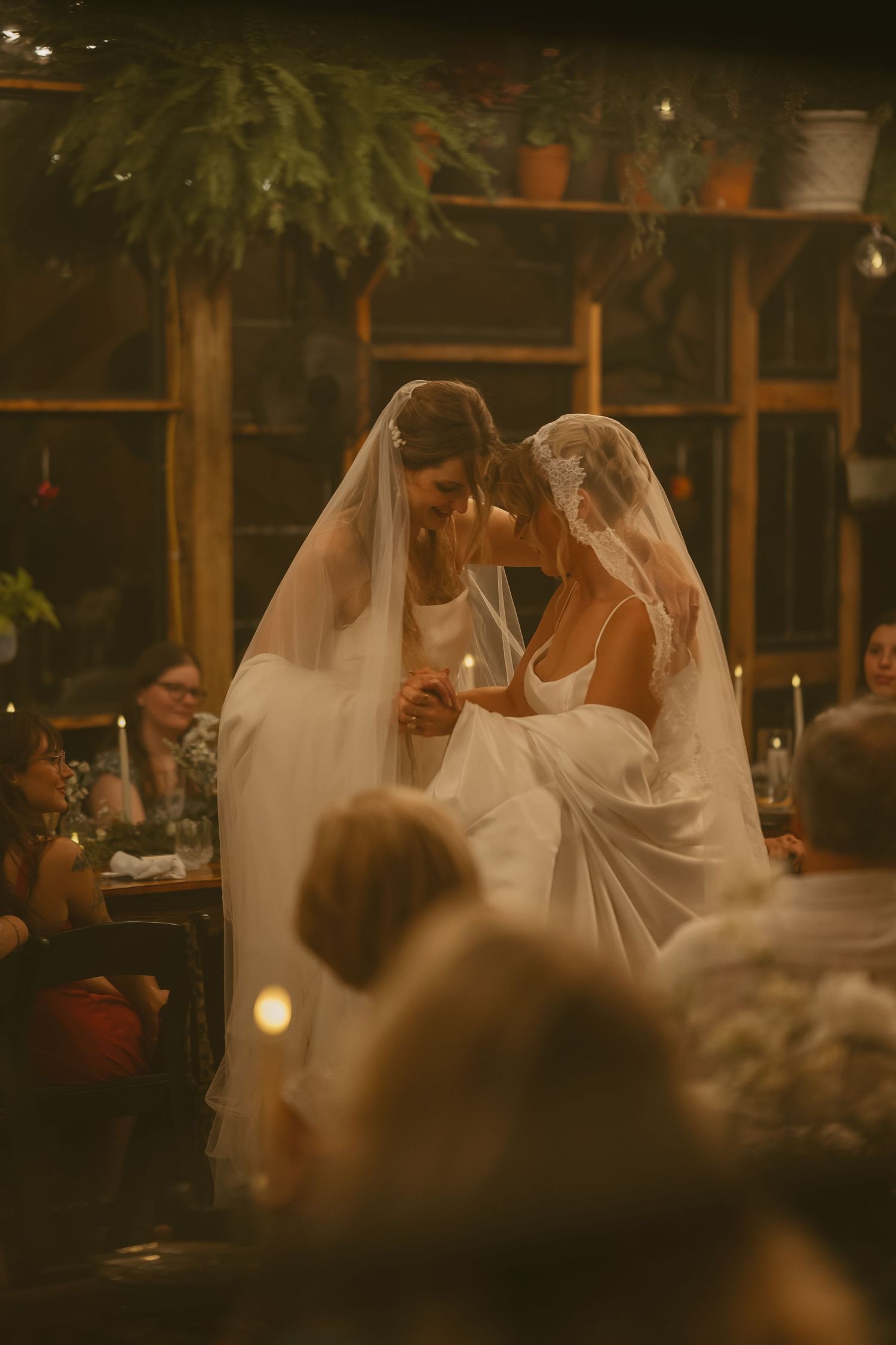 Wedding ceremony scene in a dimly lit rustic venue with hanging lights creating an intimate atmosphere.