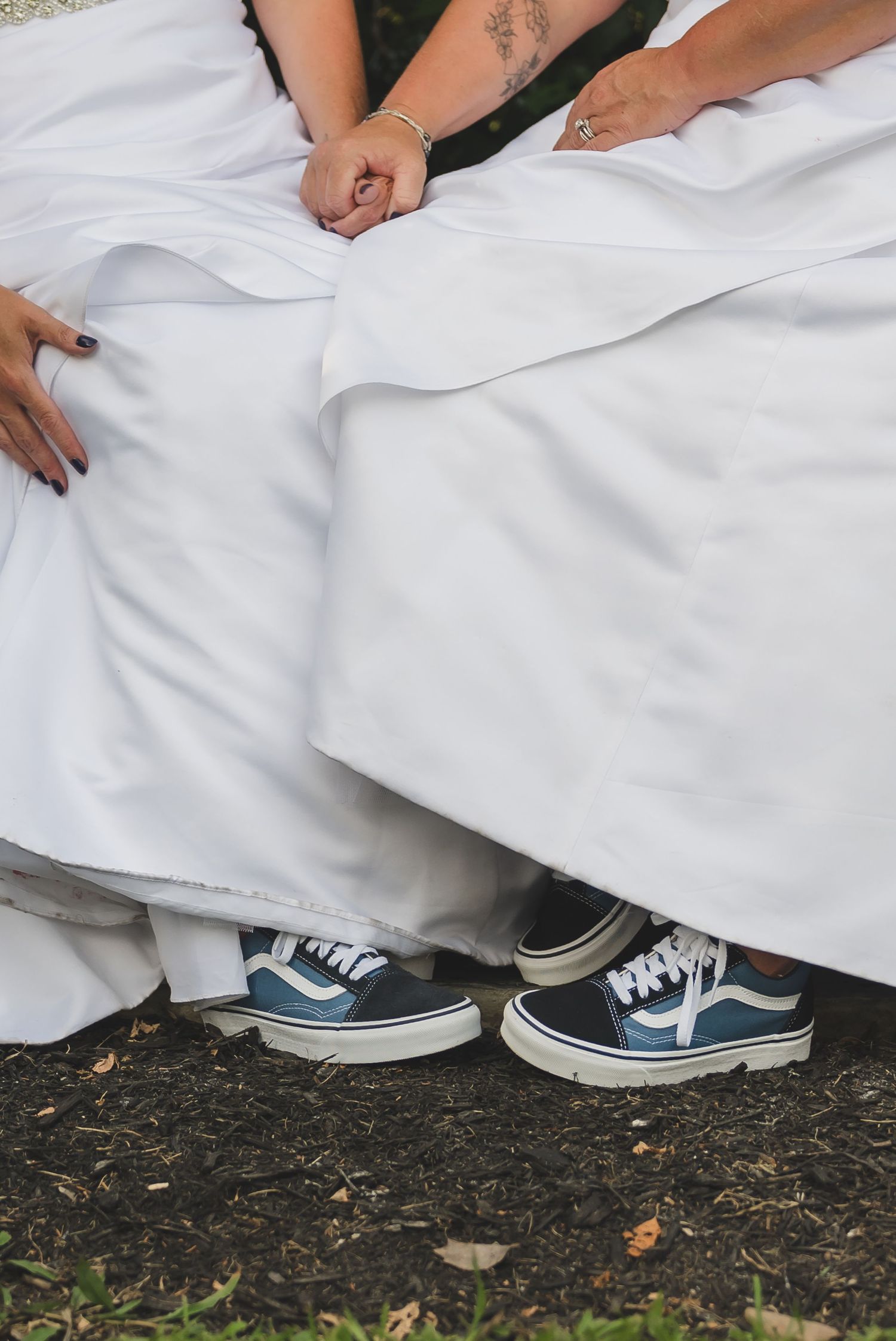 Blue sneakers peek out beneath white wedding dress fabric while sitting on the ground.