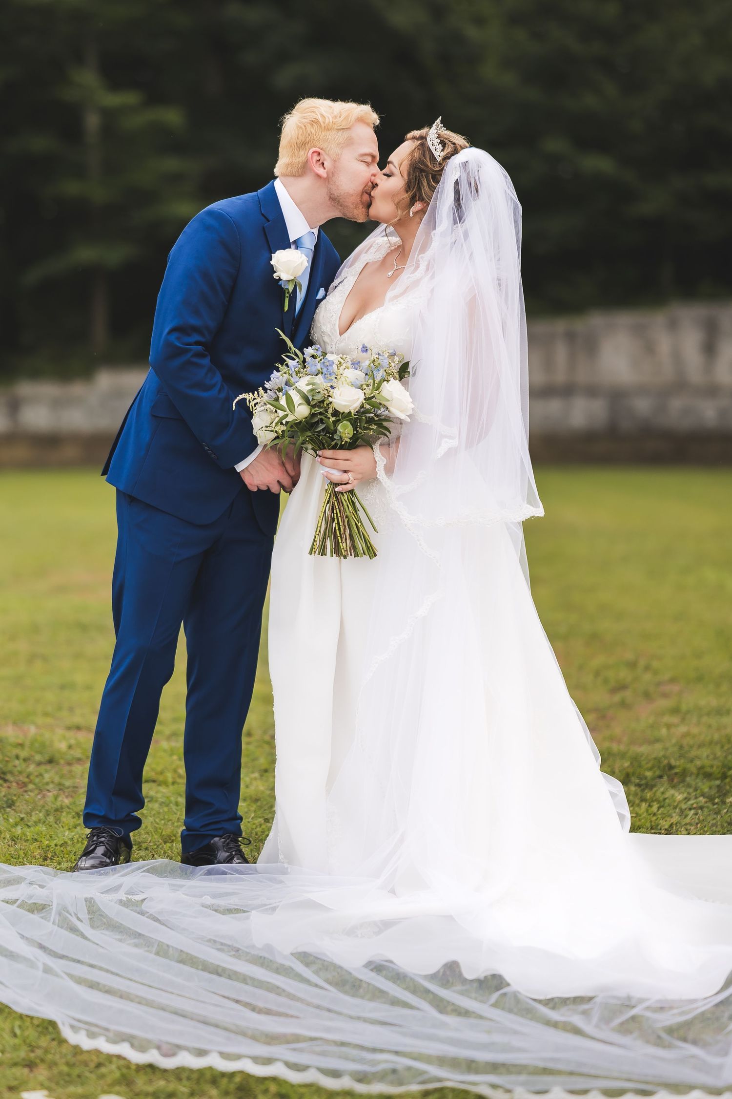 Bride and groom share intimate moment on grassy lawn with flowing white wedding dress train.