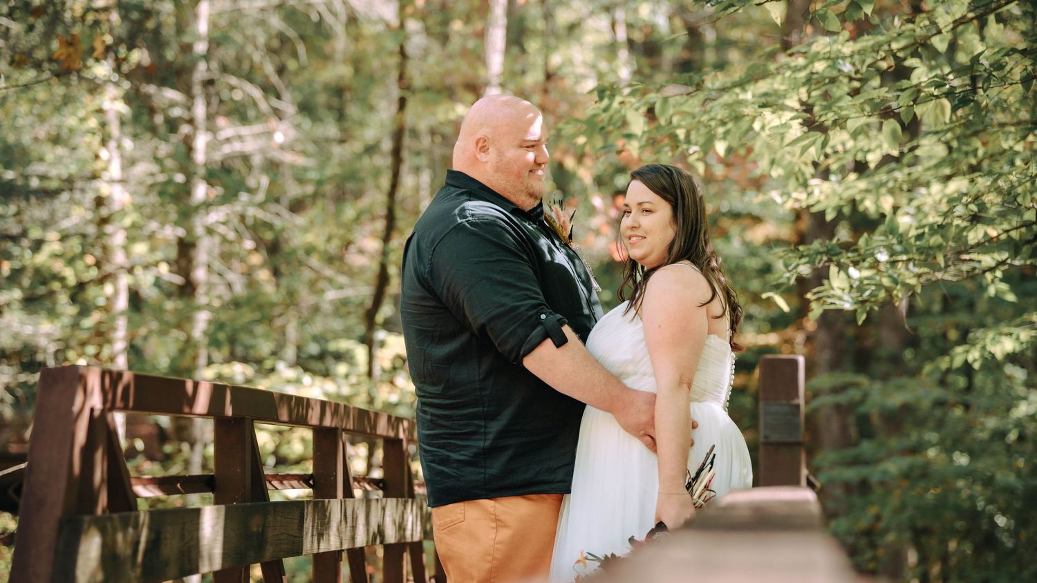A romantic couple shares tender moments in multiple photos along a rustic wooden boardwalk surrounded by lush forest.