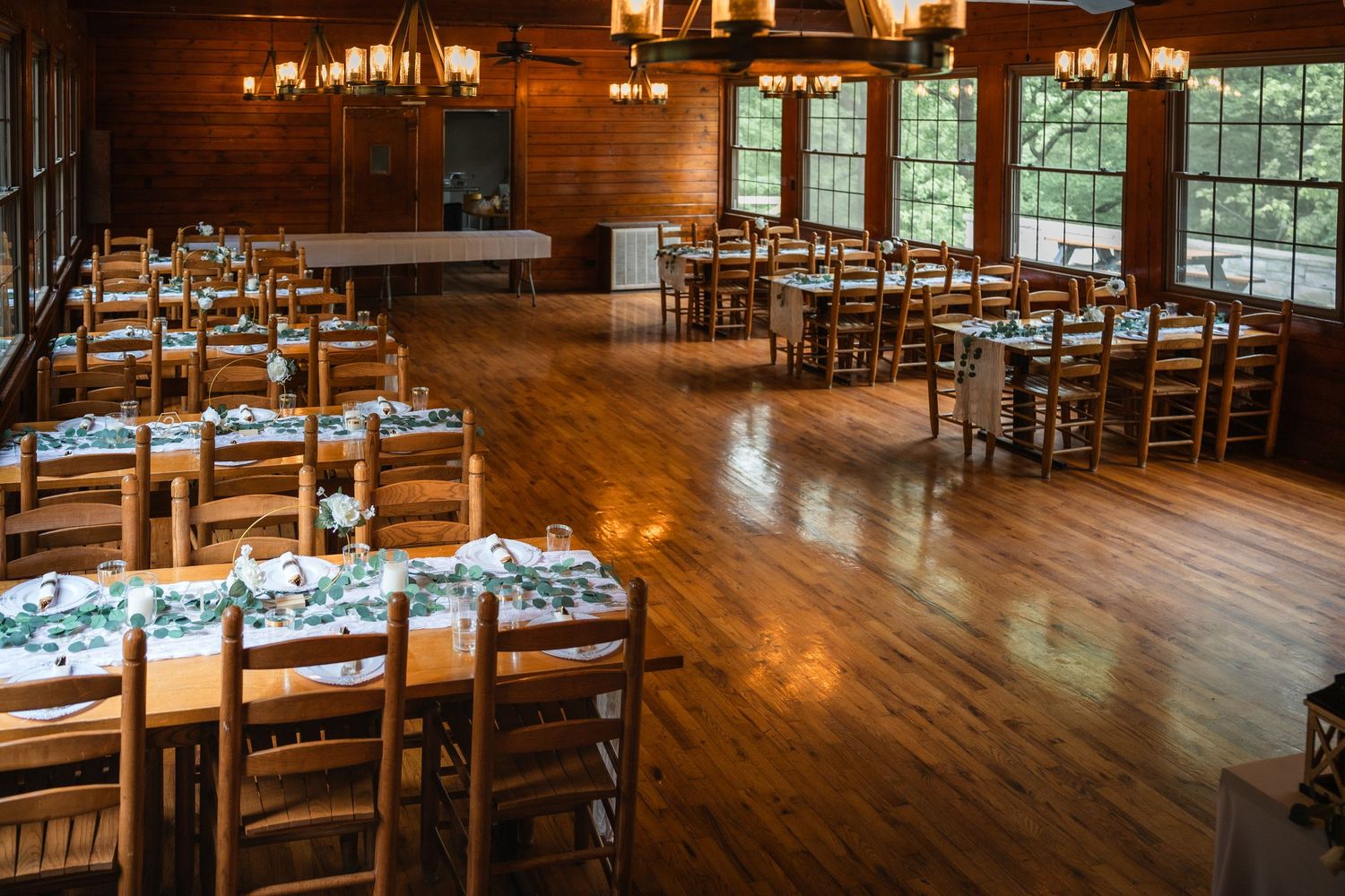 Rustic wooden reception hall with elegant table settings and large windows overlooking natural scenery.