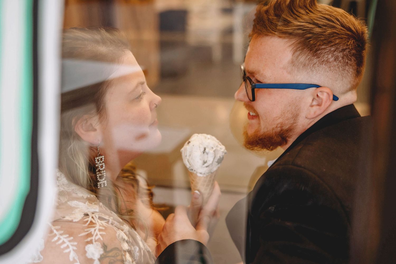 Two people enjoying ice cream cones while sitting by a window.