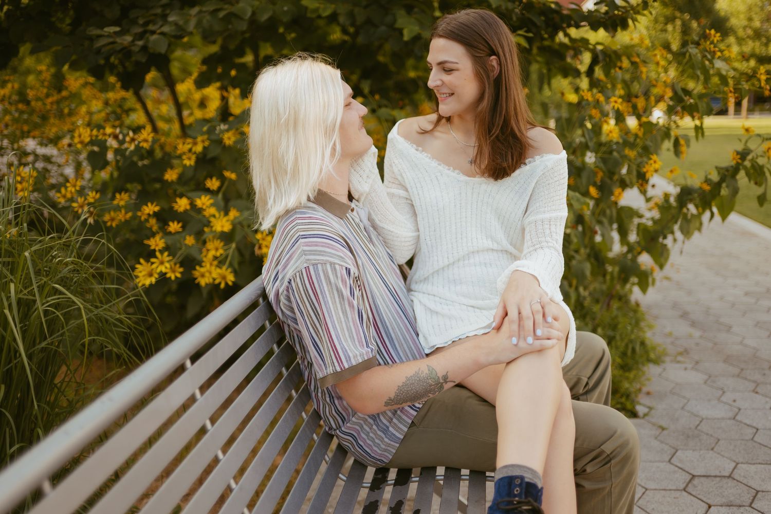 A couple sits close together on a wooden bench in a park during golden hour sunset lighting.