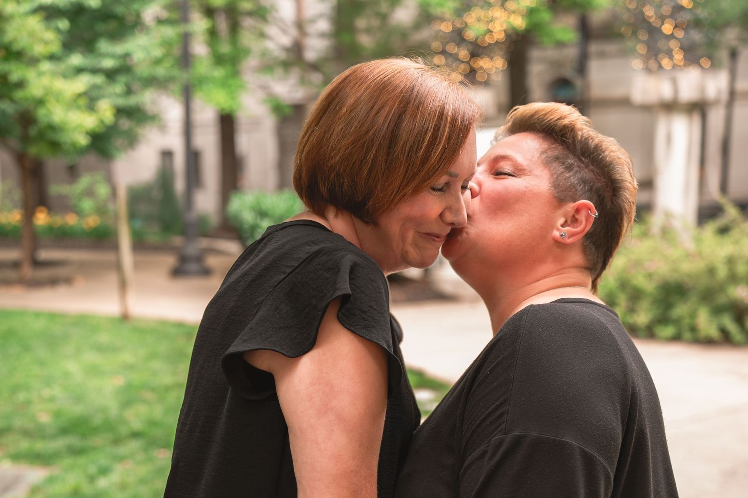 Two people share a romantic moment together in a garden setting with lush greenery in the background.