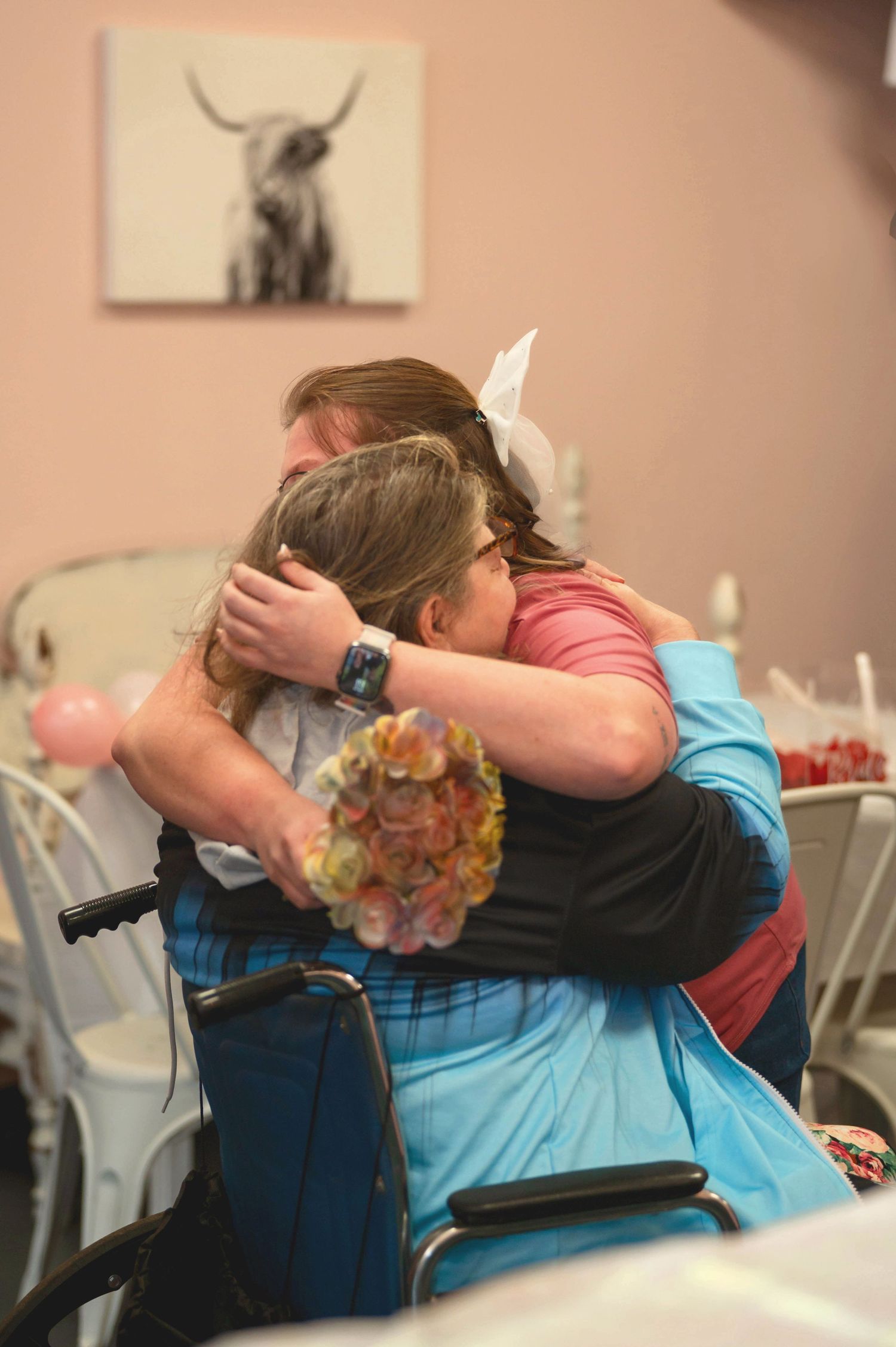 An emotional embrace takes place at an indoor event with a highland cow painting visible on the wall.