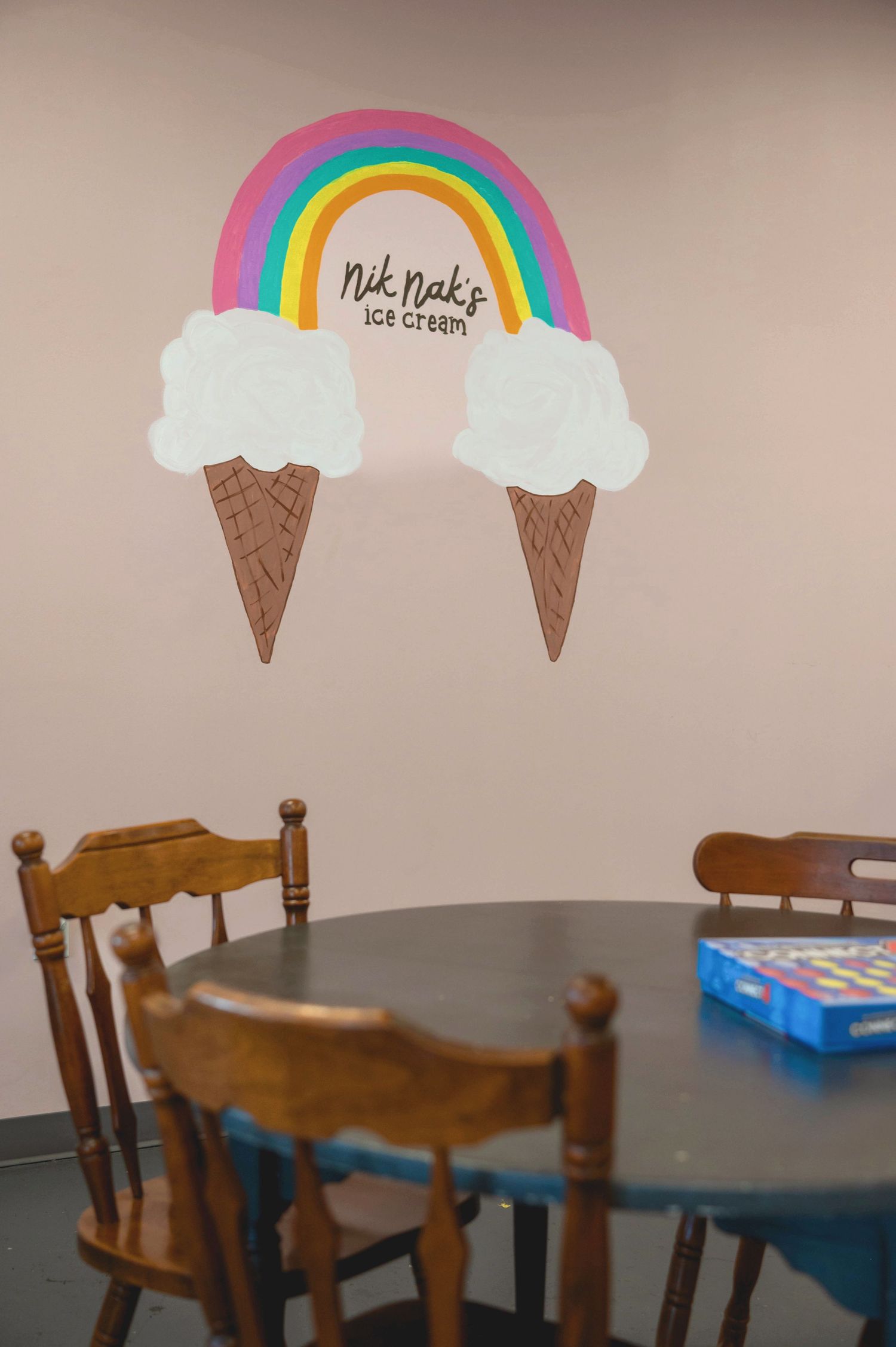 Wall art featuring two ice cream cone clouds connected by a colorful rainbow in a dining room.