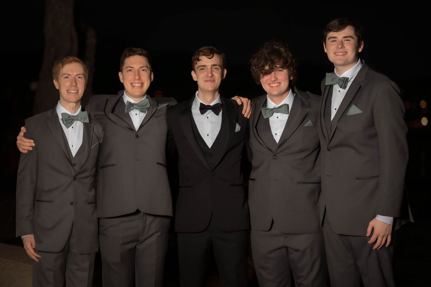 Five people in matching brown suits and black bow ties pose together at a formal event.