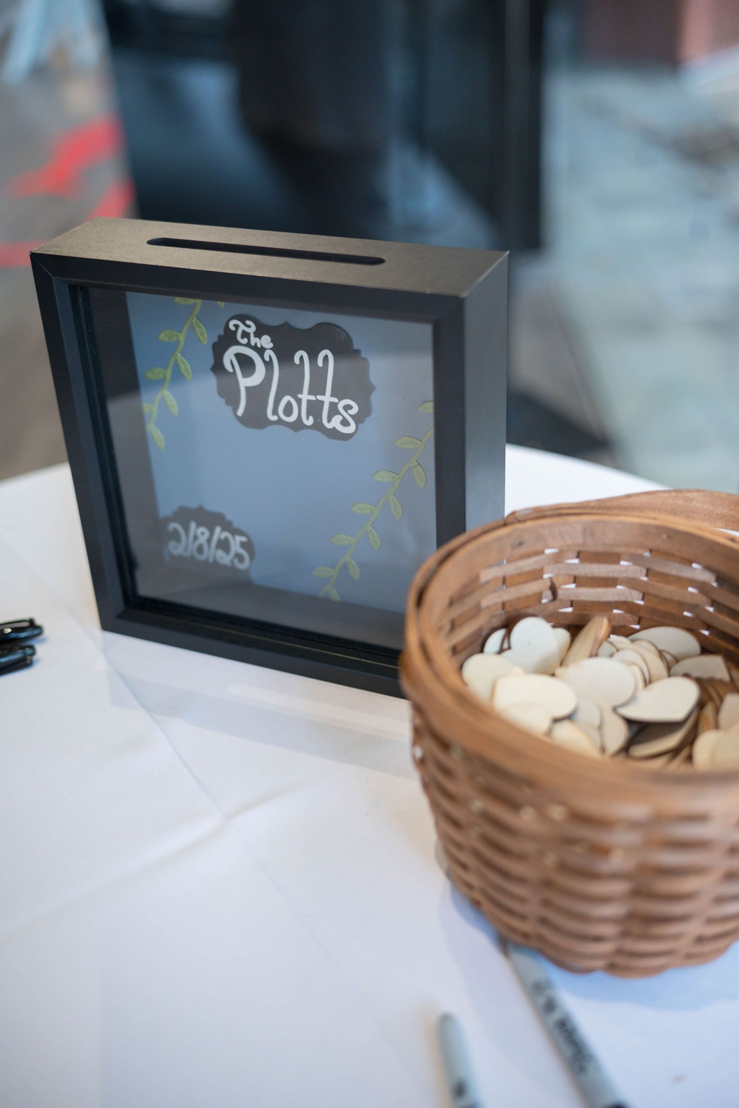 Wedding decor detail showing a labeled Plotts shadow box frame next to woven basket.