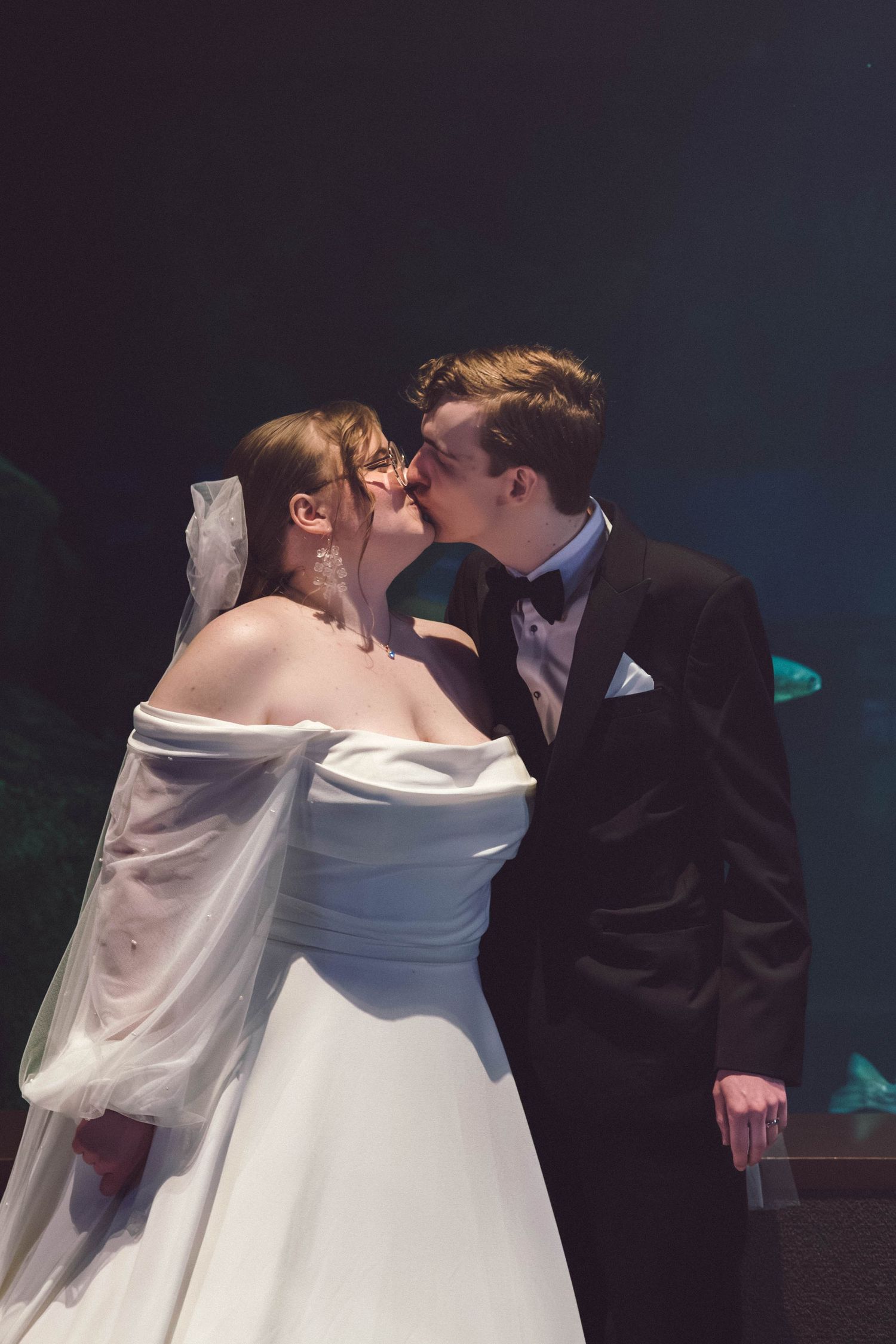 Five sequential wedding photos showing the romantic kiss between newlyweds at a dimly lit indoor ceremony.