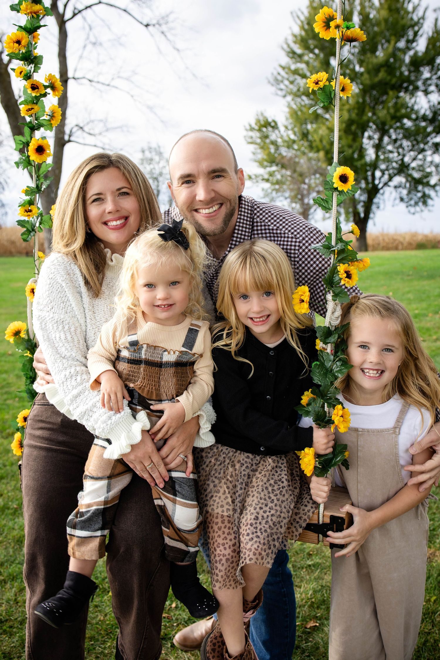 Happy family of five smiling together on sunflower decorated swing in autumn outdoor portrait.