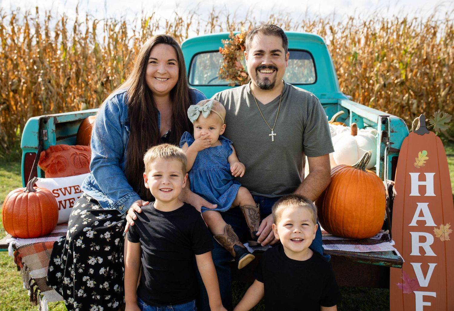 Family of five posing with vintage teal truck and pumpkins at fall harvest corn field photo session.