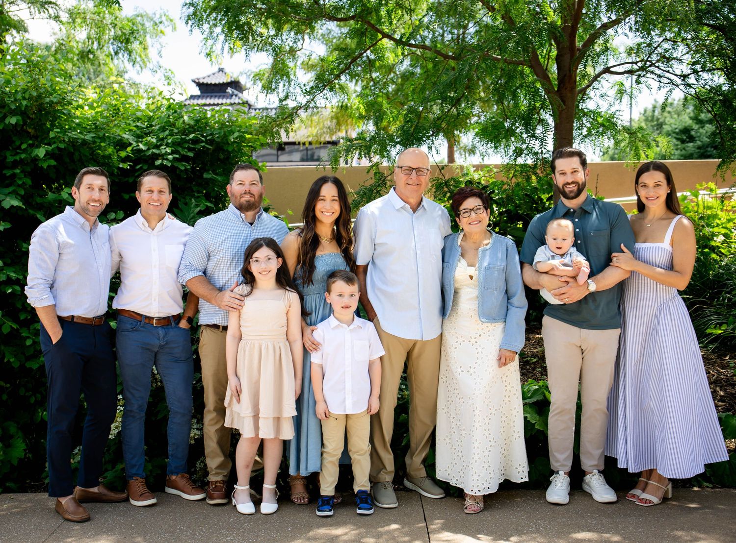 Large extended family group photo of ten people posing together in a lush garden setting.