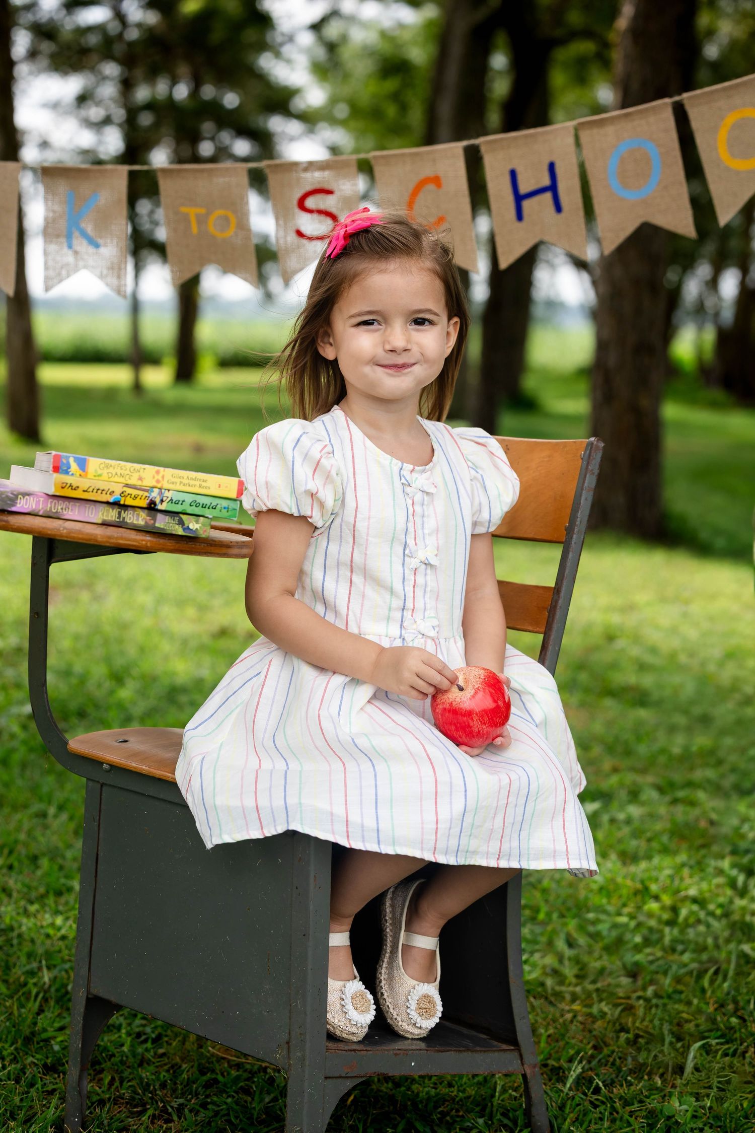 Adorable little girl in striped dress sitting at school desk with apple for back to school portrait.