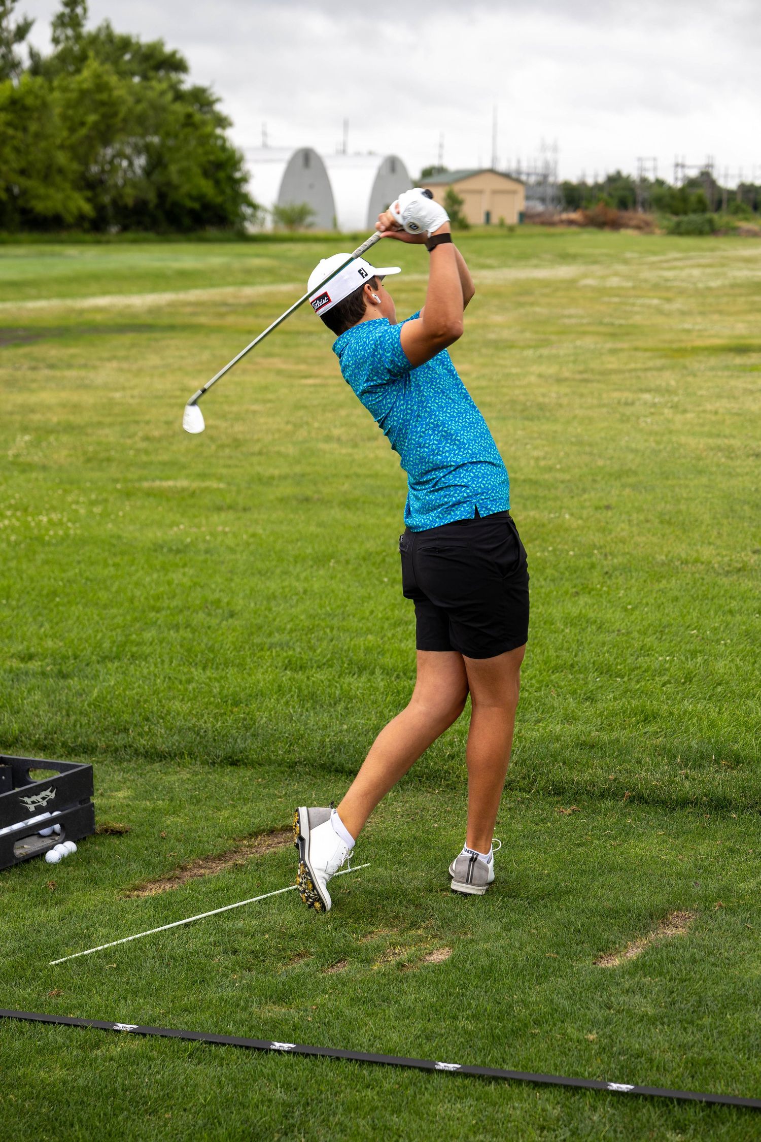 Female golfer in blue shirt completes a full golf swing on a green driving range.