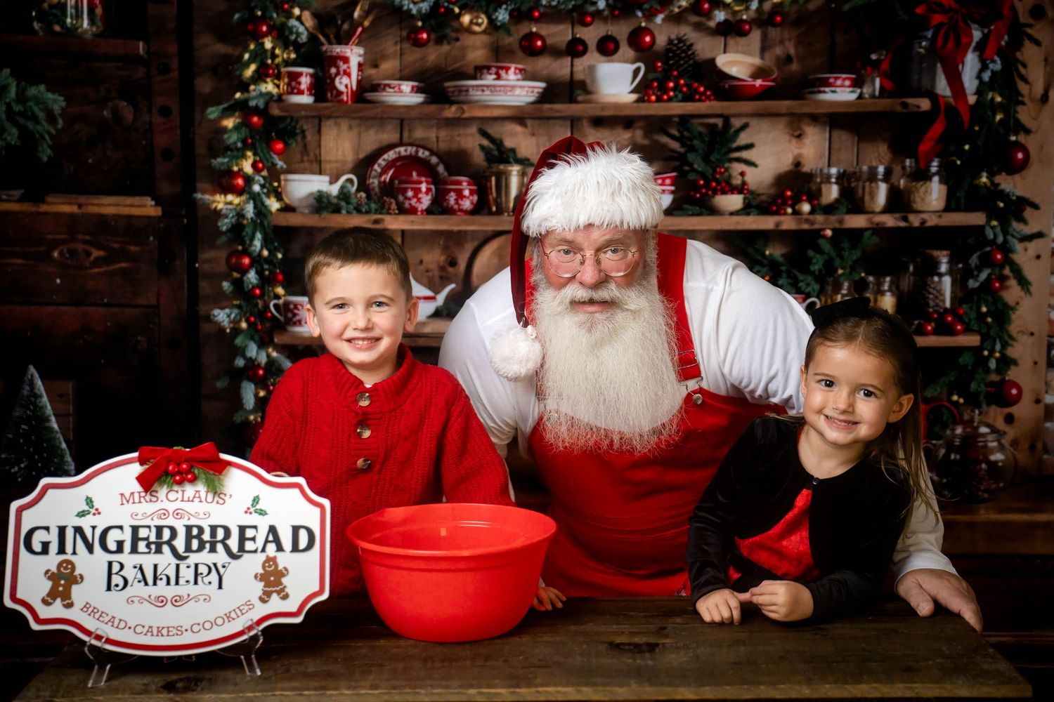 Two children pose with Santa Claus at a festive Gingerbread Bakery Christmas photo set.