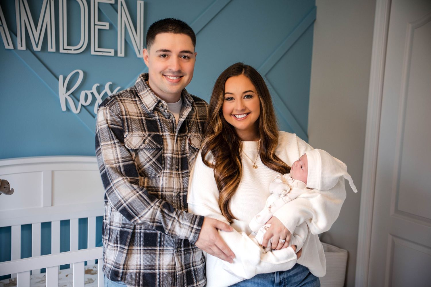 Proud parents smiling with their newborn baby in a nursery with Camden Ross name sign.