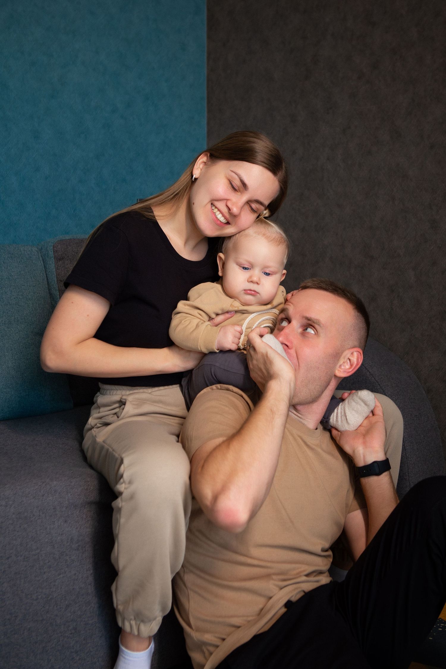 A heartwarming series of candid moments between a parent and baby playing together on a gray couch against a dark backdrop.