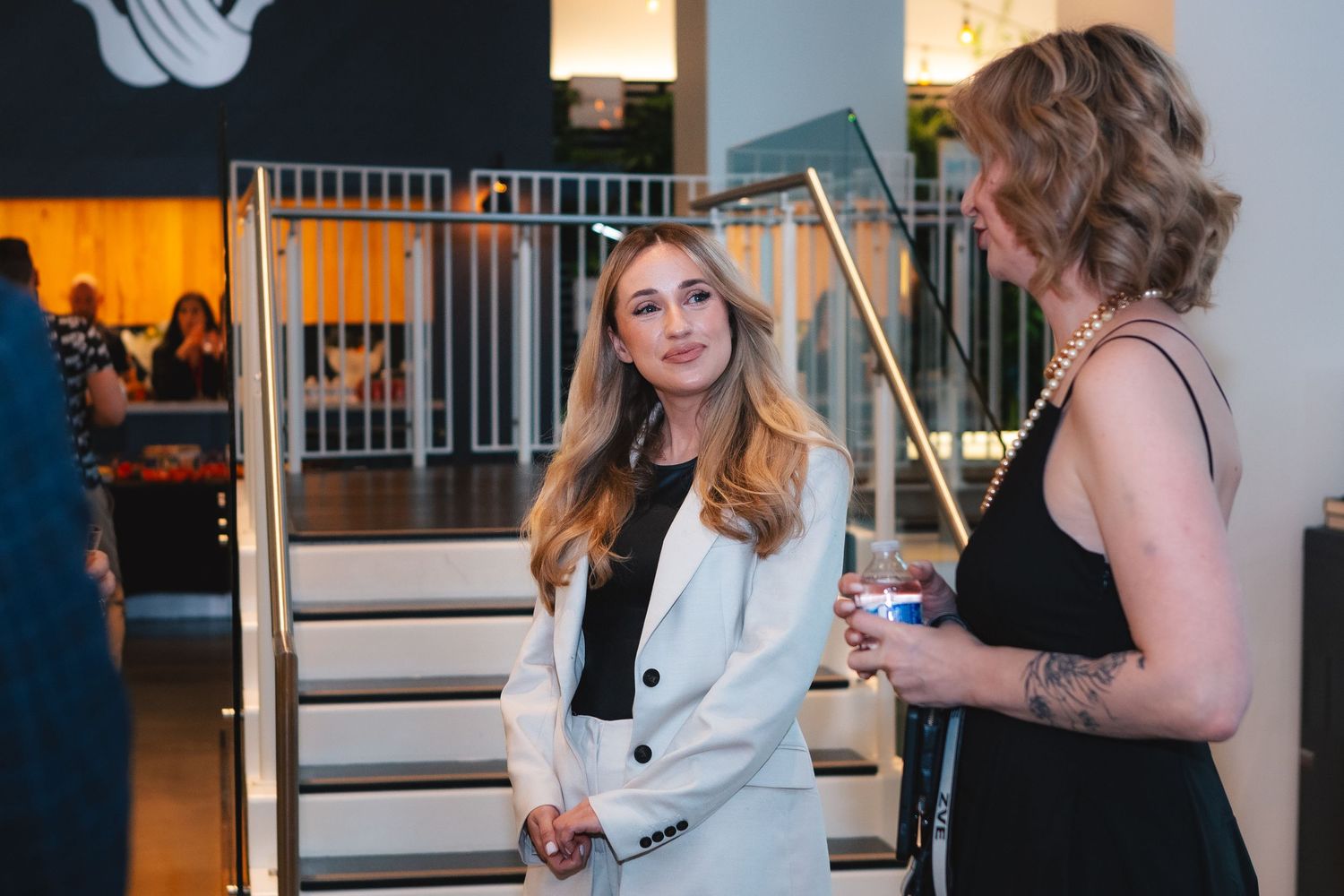 Two people having a conversation beside a staircase in a modern office space with ambient lighting.