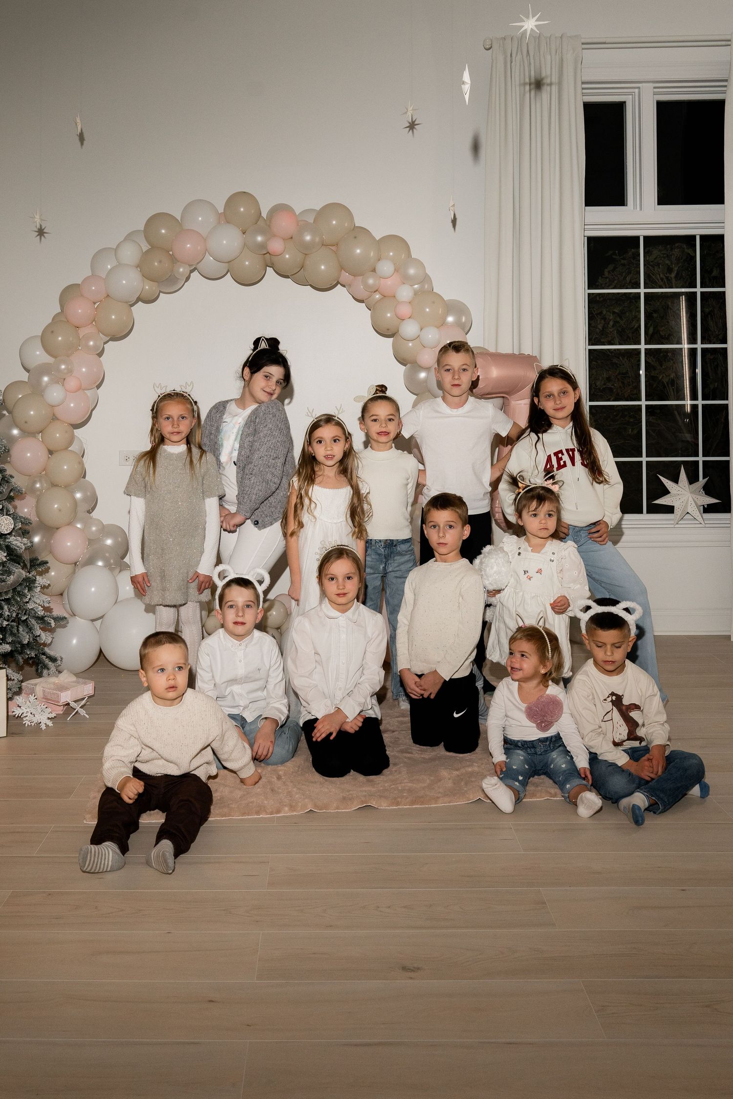 Large group photo under a festive balloon arch with people wearing white and neutral colored outfits.