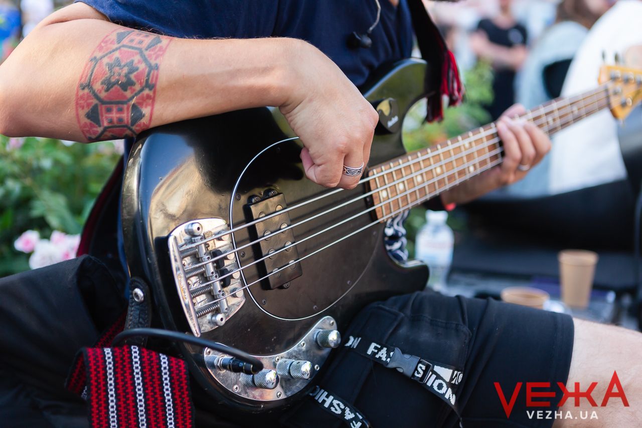 Close-up of tattooed hands playing bass guitar during live performance.