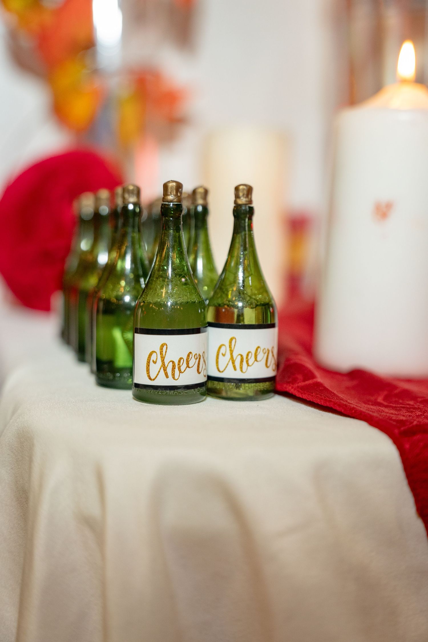 Row of green bottles labeled 'Cheers' displayed on white tablecloth with candle.
