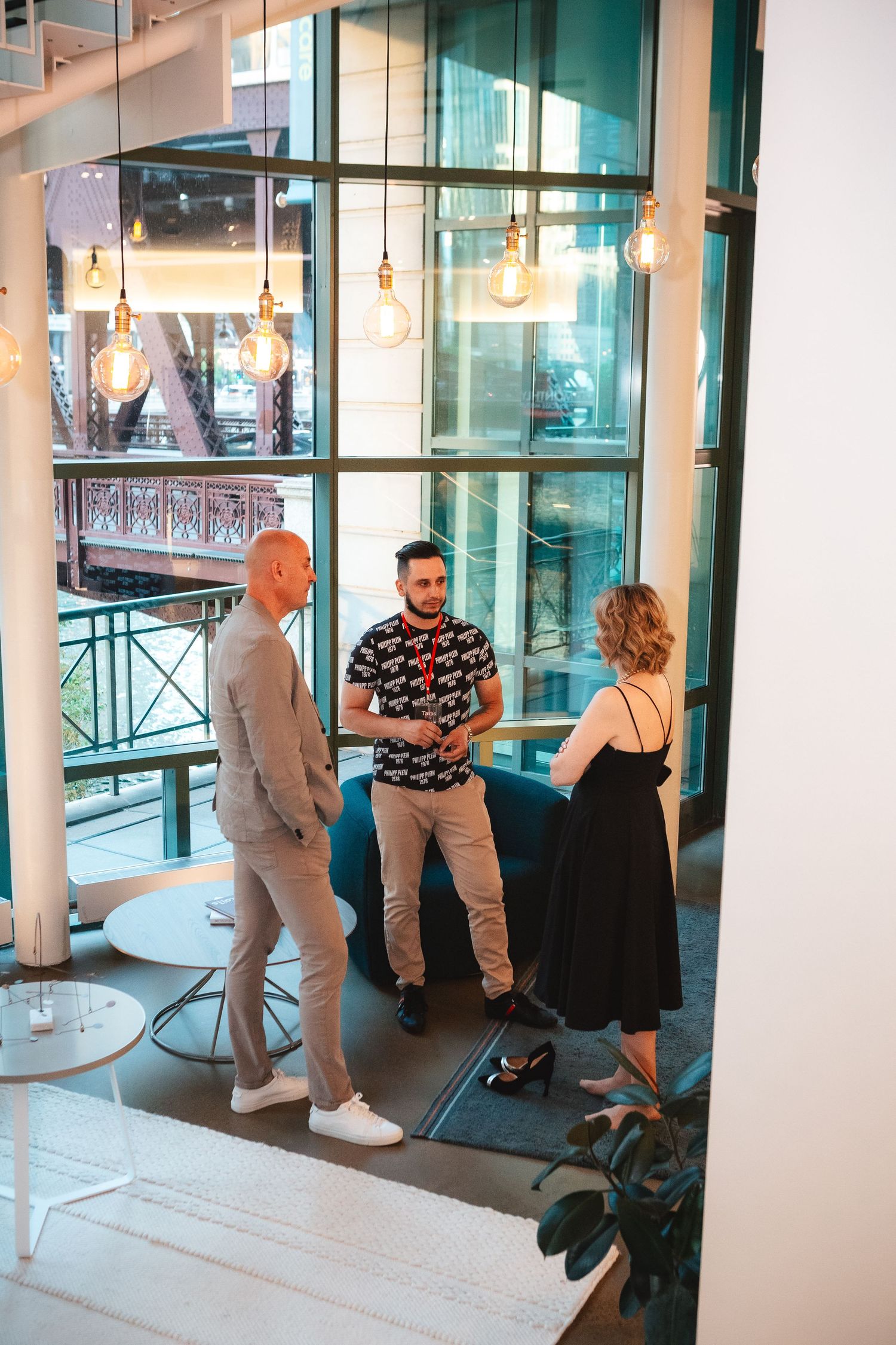 Three people having a casual conversation in a modern office space with hanging pendant lights.