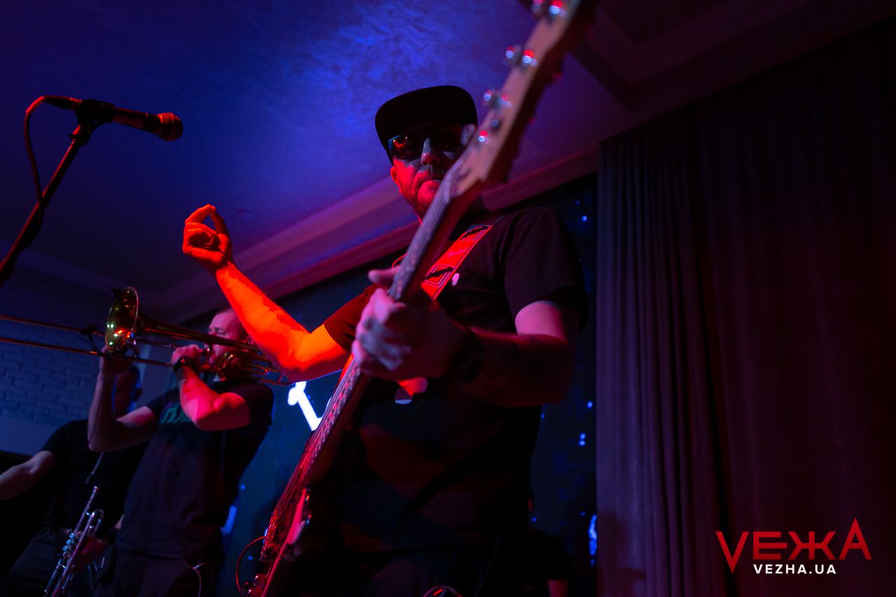 Musicians perform on stage with red and blue lighting effects.