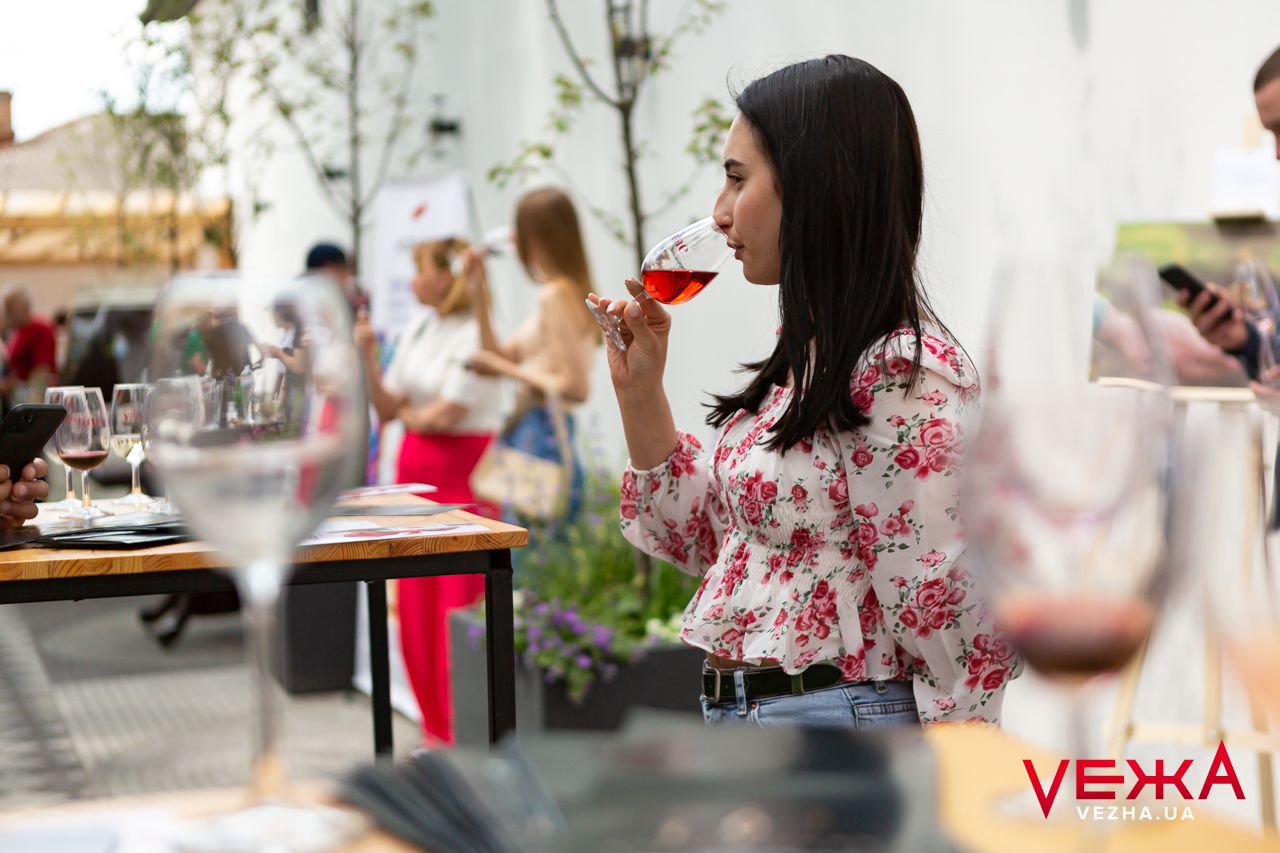 A person enjoys wine on an outdoor patio during a sunny afternoon with floral decor.