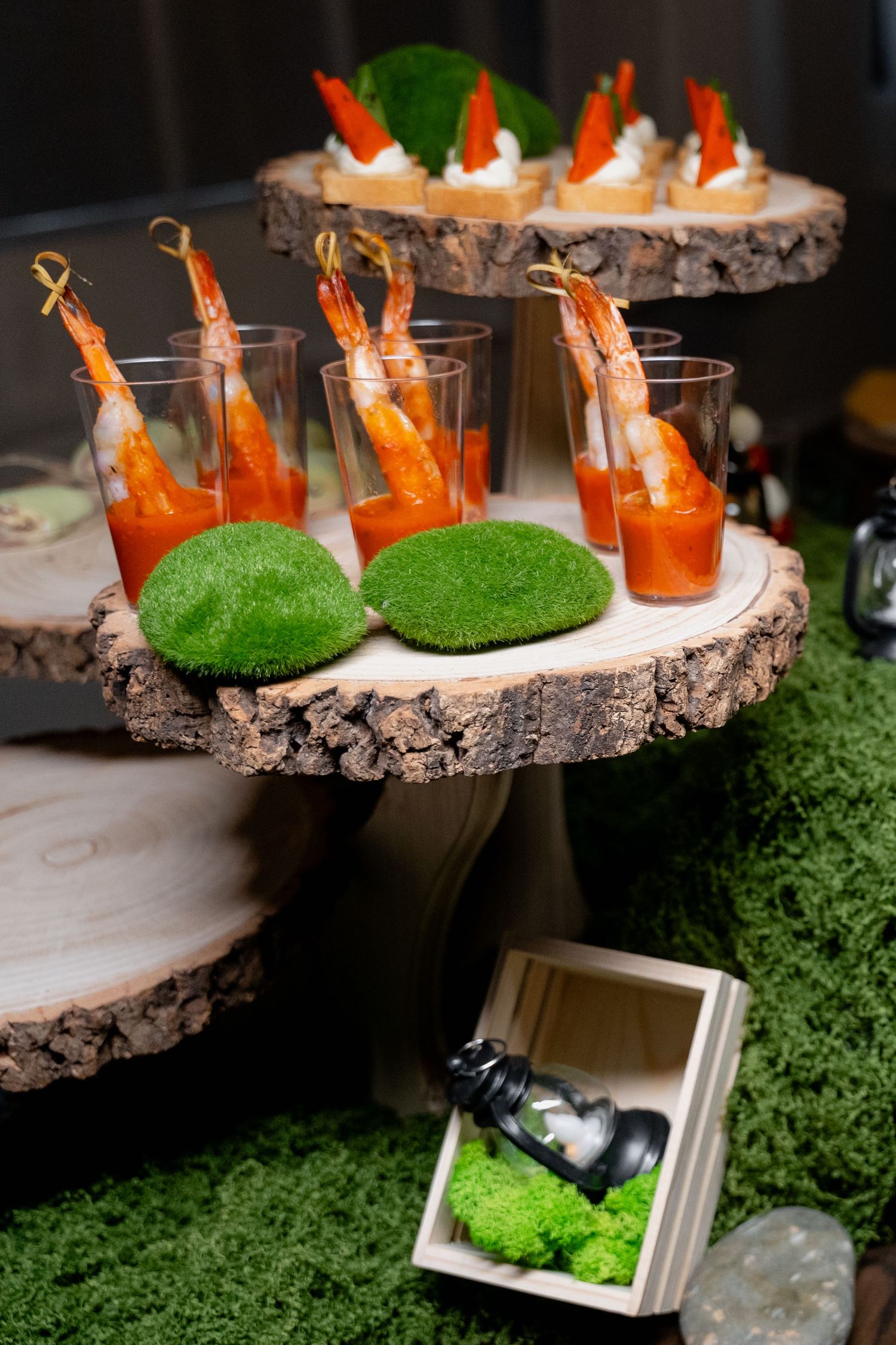 Decorative appetizer display featuring shrimp cocktails on rustic wood slices with moss accents.