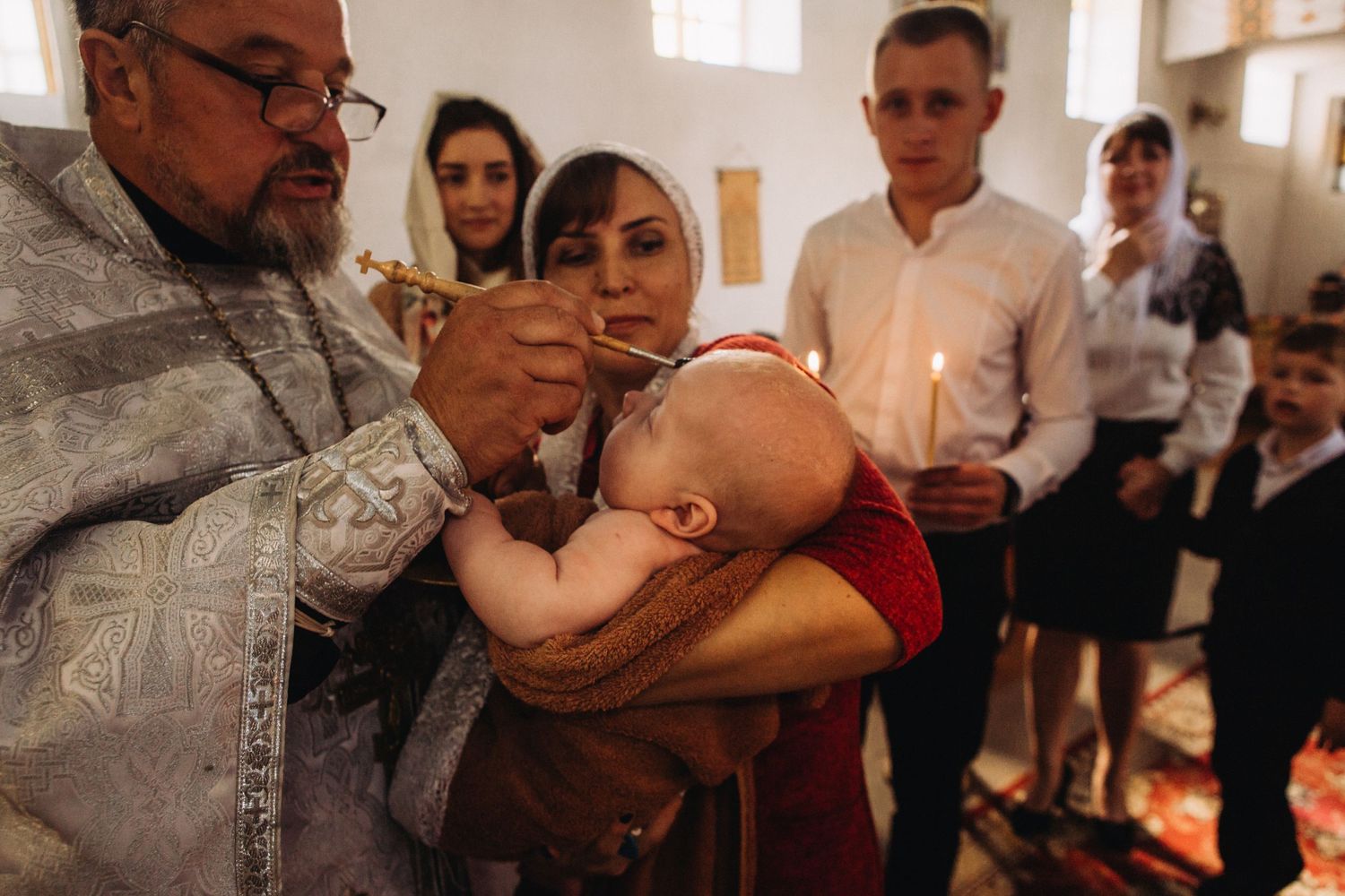 Orthodox baptism ceremony with clergy member performing sacrament in church.