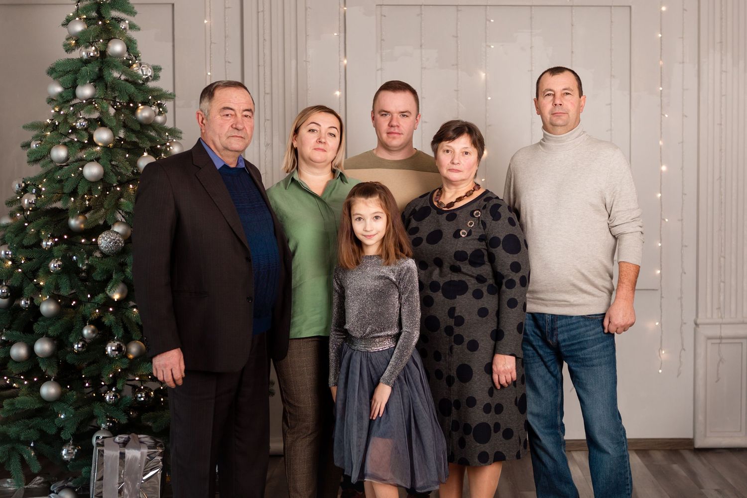 Multi-generational family poses together by decorated Christmas tree in studio setting.